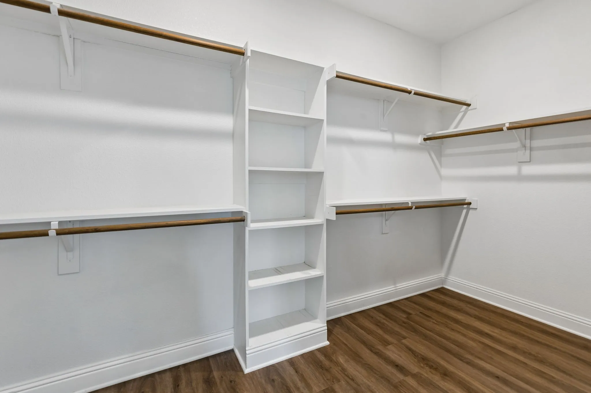 Walk-in closet with built-in shelving, multiple hanging rods, and wood-finish flooring