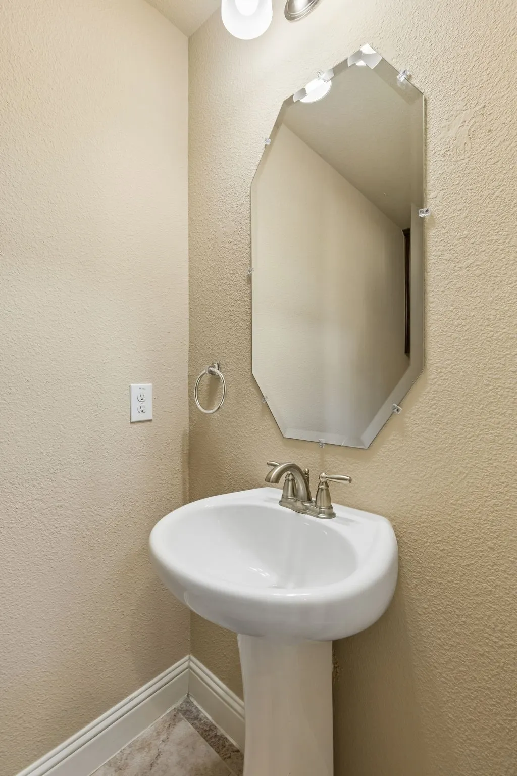 Pedestal sink with brushed nickel faucet, illuminated by an overhead light fixture
