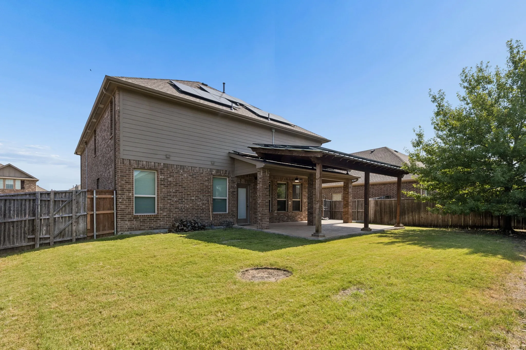 Expansive backyard featuring a covered patio, brick exterior, solar panels, and a wood privacy fence