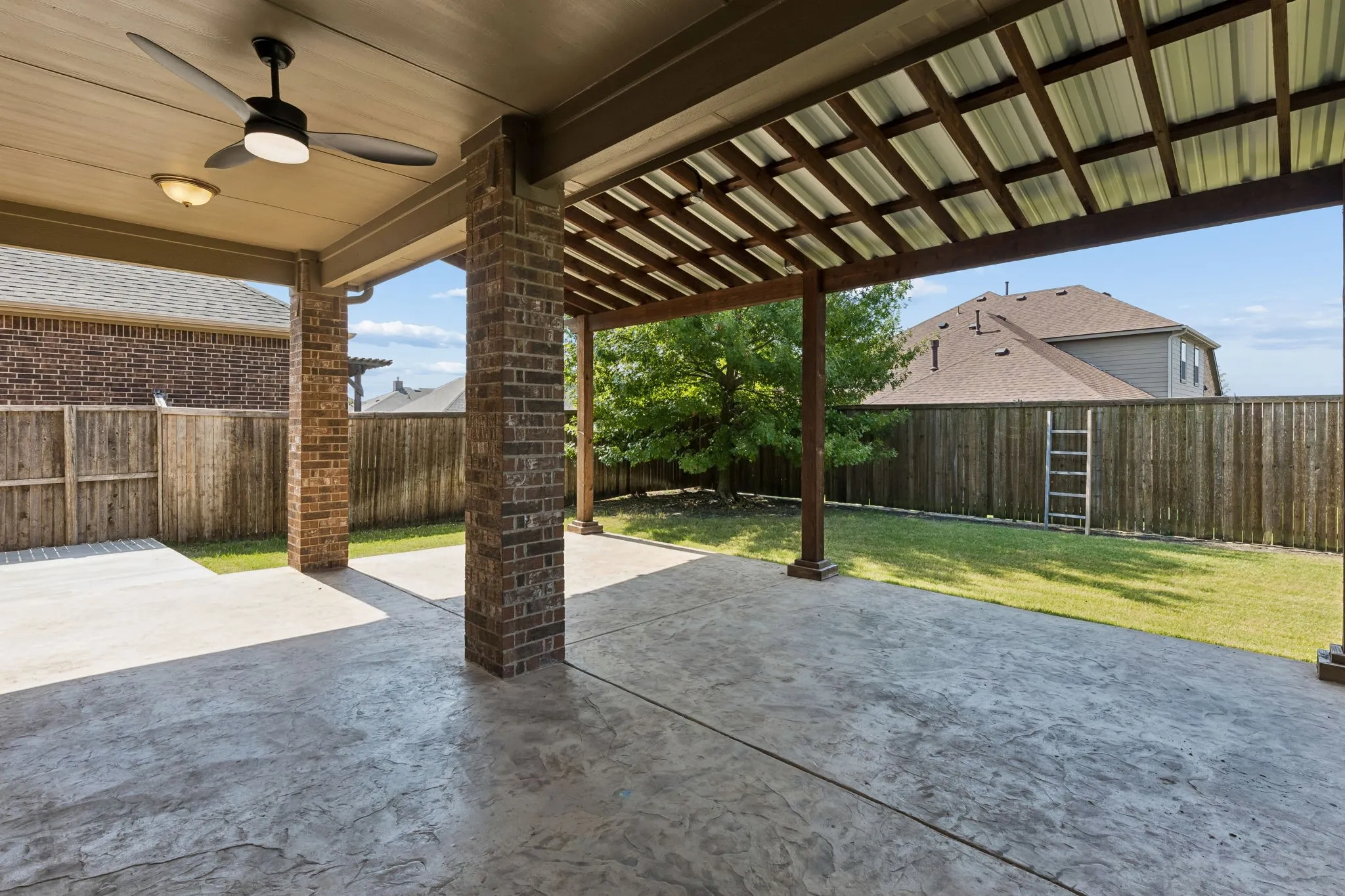 Expansive stamped concrete patio with brick support columns, an integrated ceiling fan, and a wood-slat pergola extension