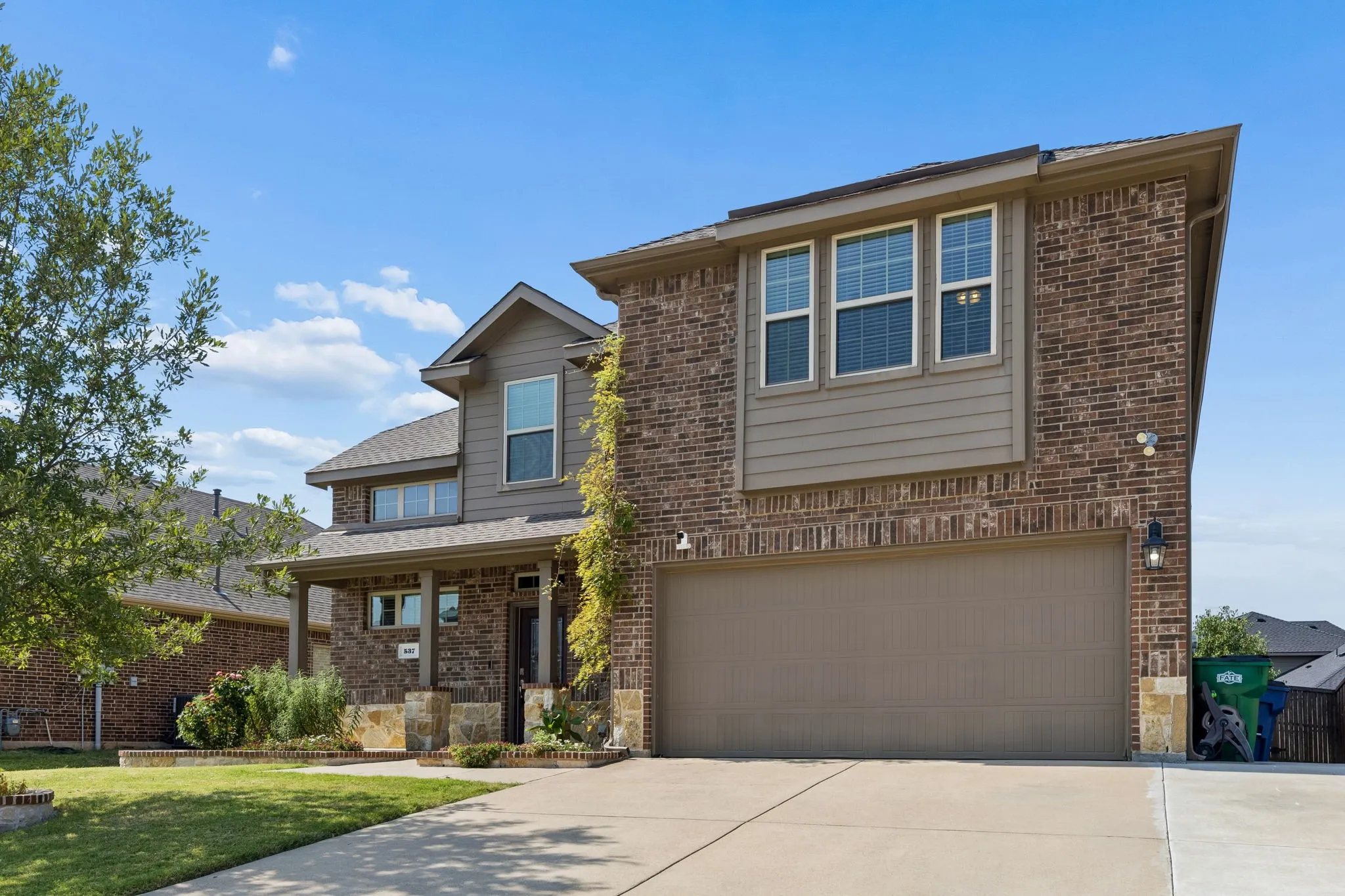 Two-story exterior with brick and siding facade, covered front porch, attached garage, and concrete driveway
