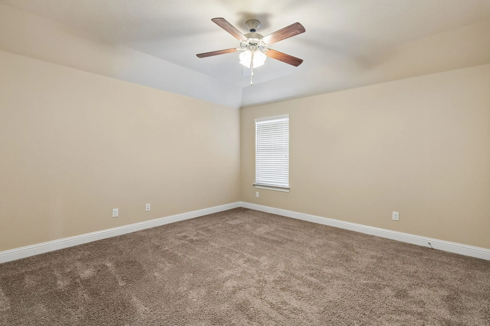 Neutral tone wall paint, textured carpet flooring, window with blinds, ceiling fan with light fixture, and a tray ceiling