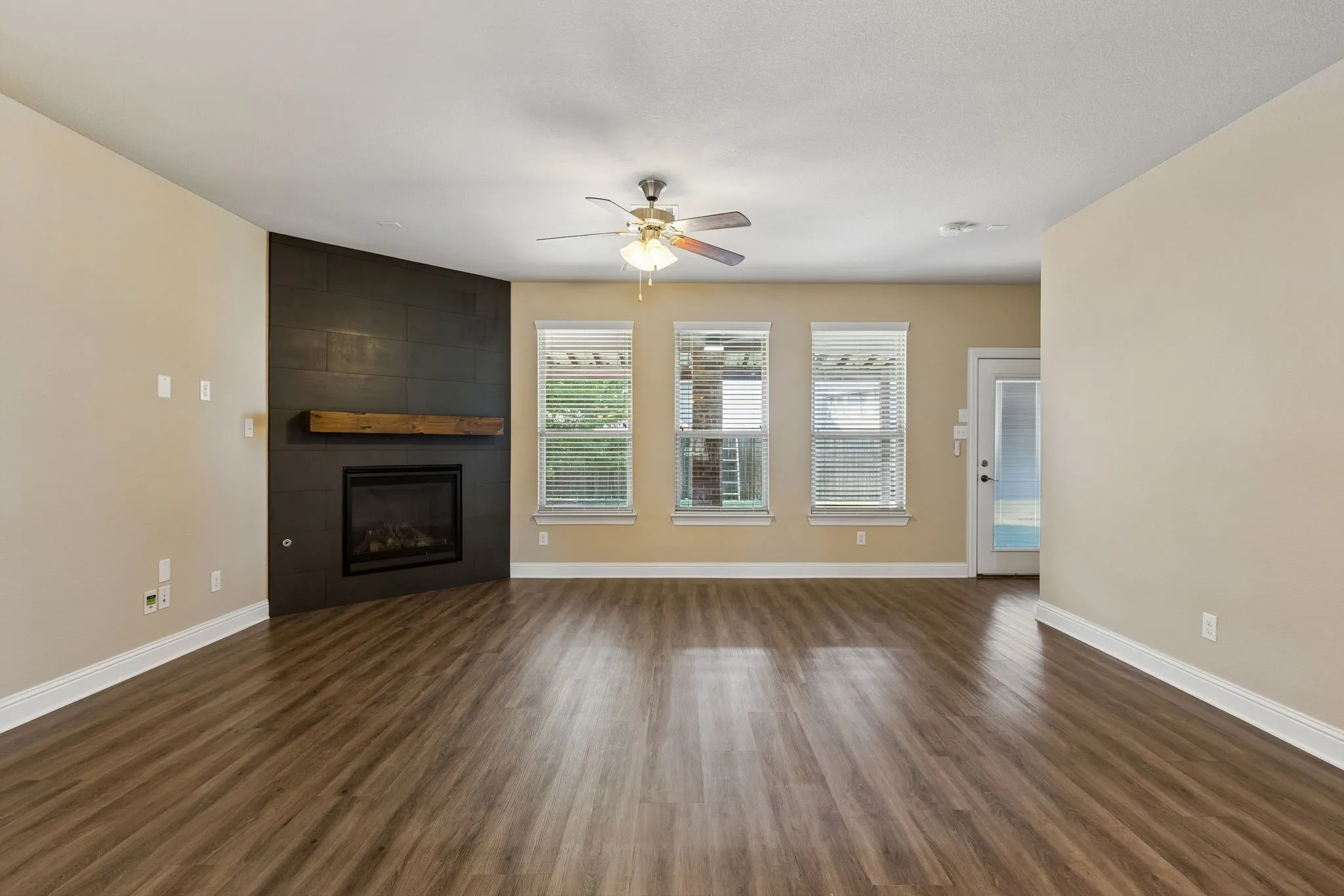 Wood-finish flooring, a ceiling fan, and a built-in fireplace with a wooden mantel