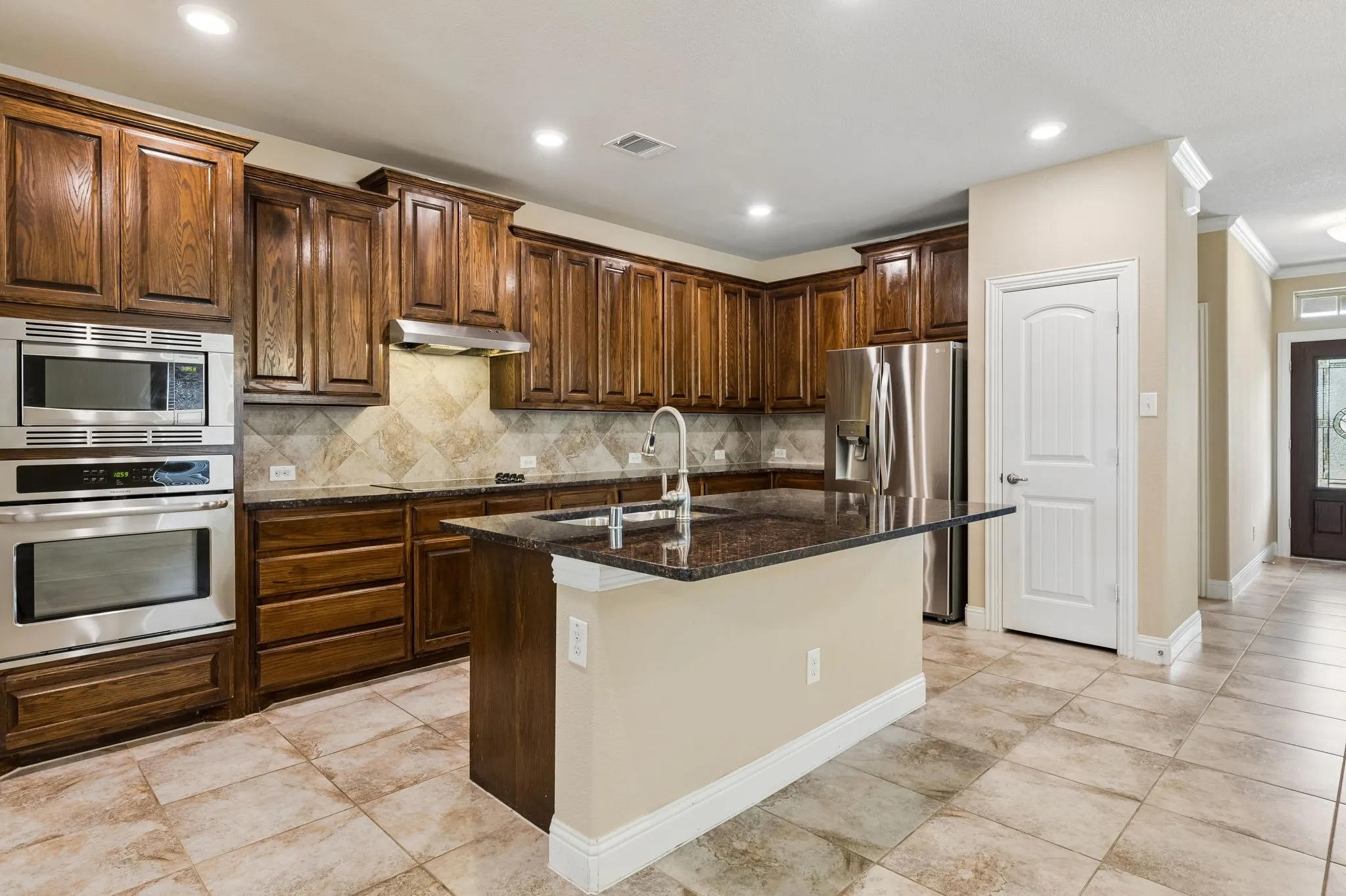 Kitchen featuring dark wood cabinetry, stainless steel appliances, a center island with a sink, stone countertops, and tile flooring