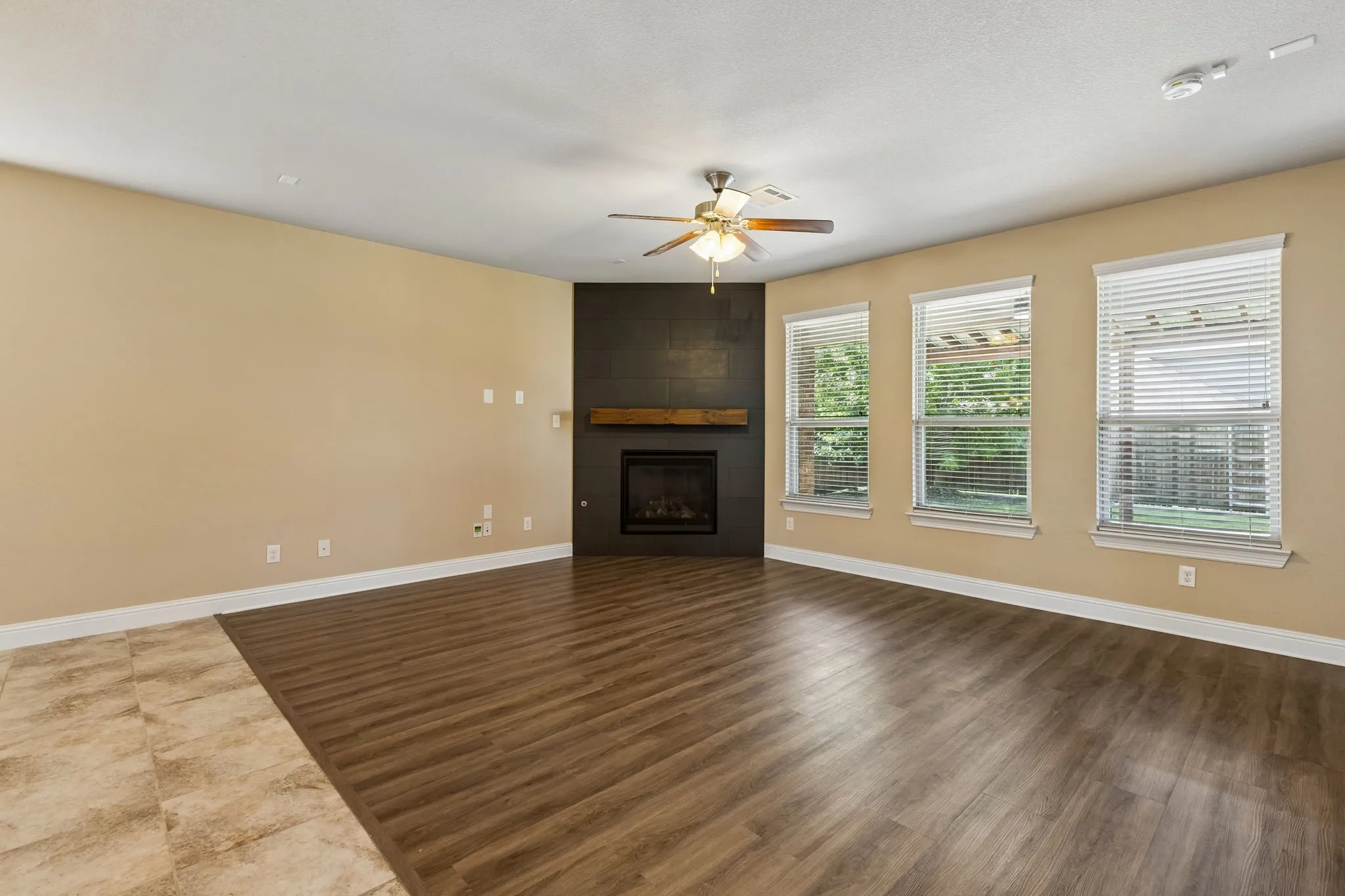Wood-finish flooring with a tiled entry, a built-in fireplace with a wood mantle, and three windows with blinds