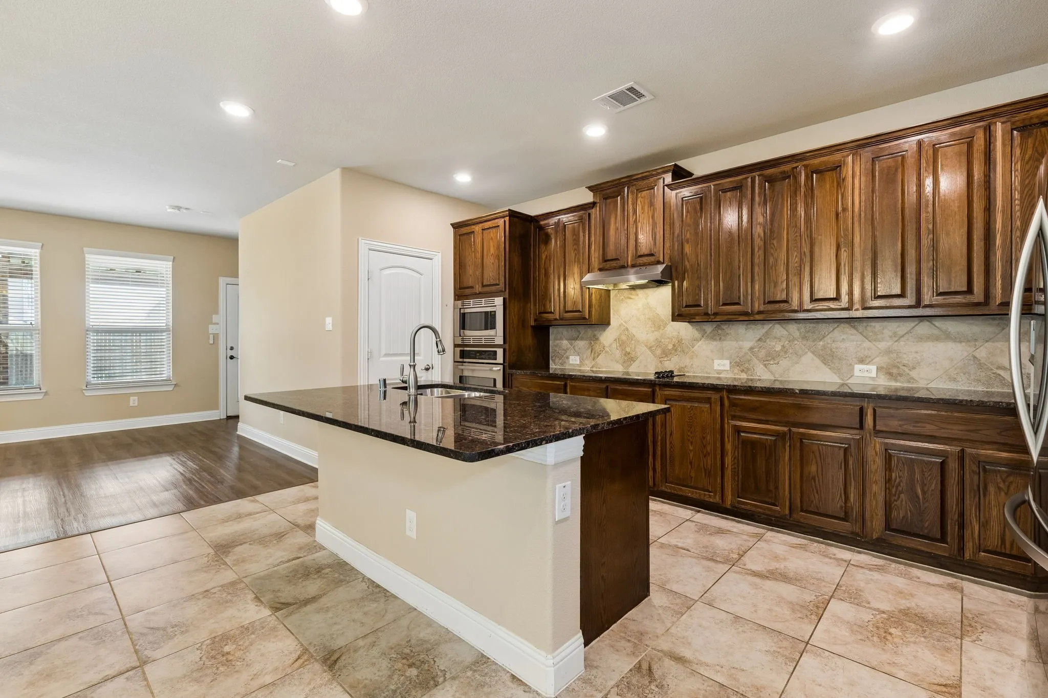 Kitchen featuring a center island with a sink, dark wood cabinetry, integrated stainless steel appliances, and tile flooring