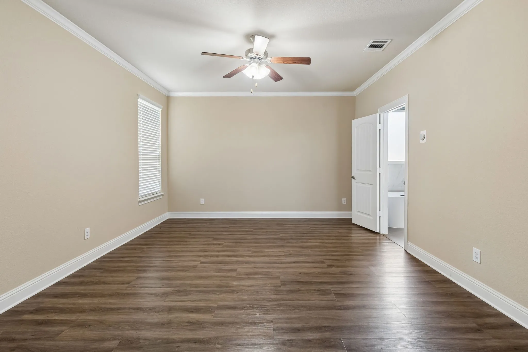Spacious room featuring wood-finish flooring, crown molding, a ceiling fan with light fixture, and a window with blinds