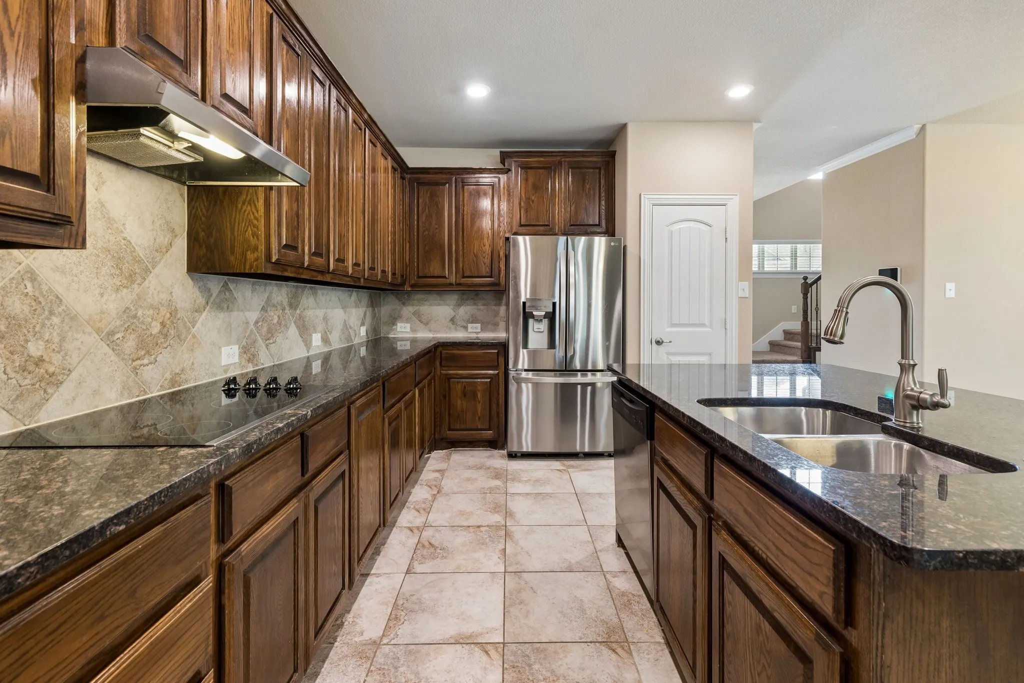 Kitchen featuring dark wood cabinetry, stainless steel appliances, granite countertops, tile flooring, and a tile backsplash