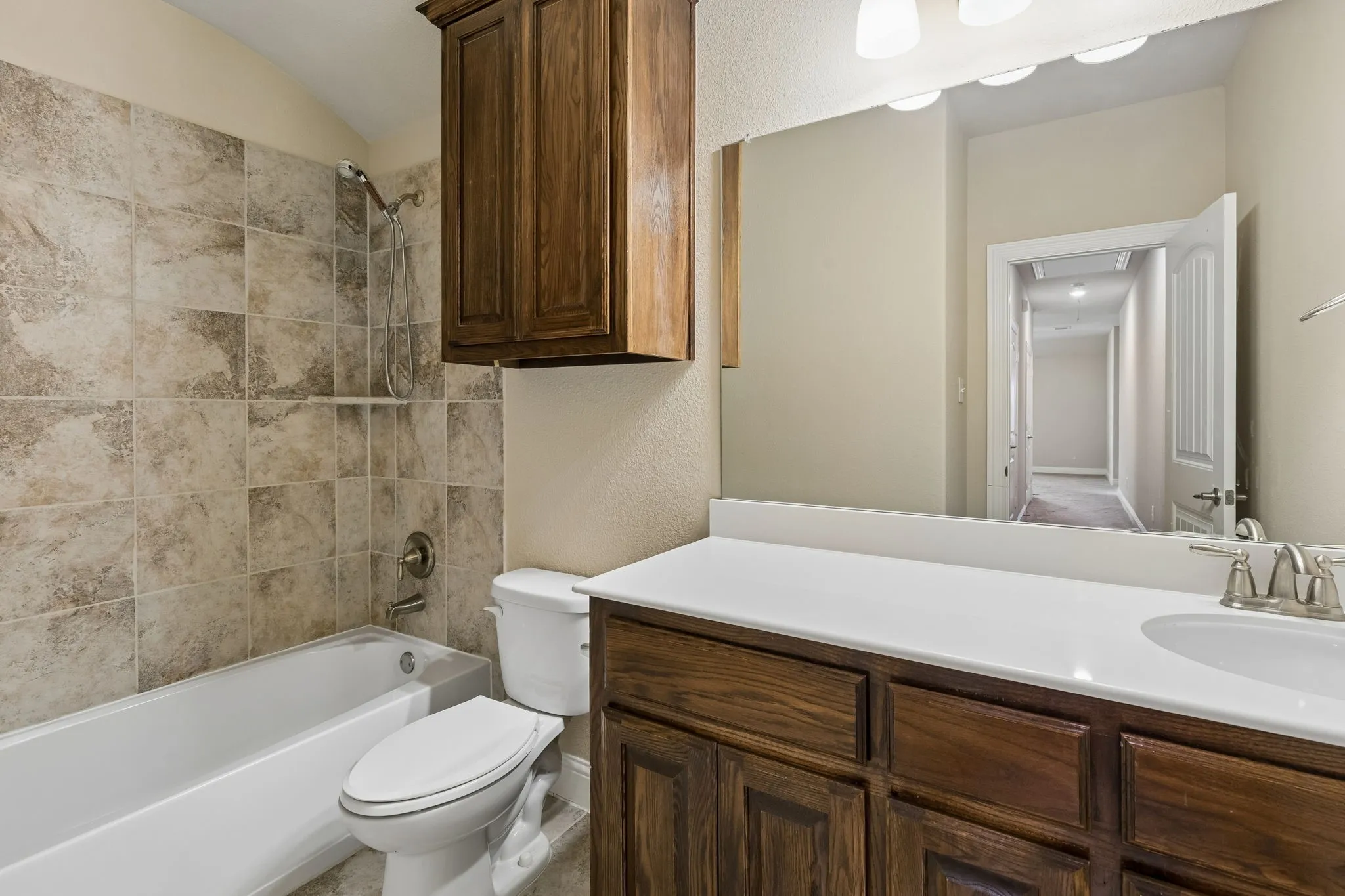 Bathroom featuring a bathtub with tiled surround, a toilet, a vanity with a white countertop and integrated sink, and an overhead mirror