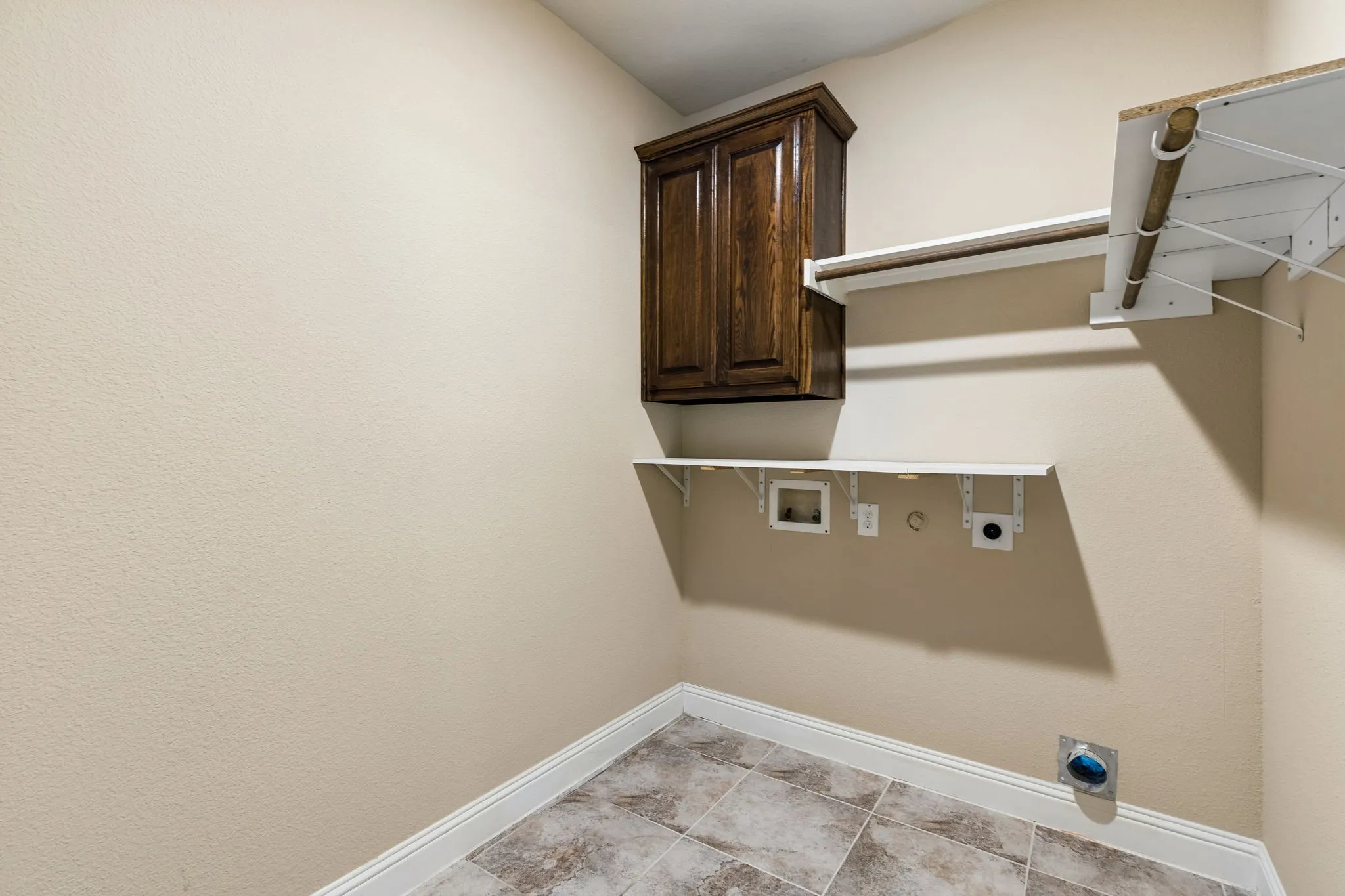 Laundry area featuring tile flooring, a wood-finish cabinet, and white shelving