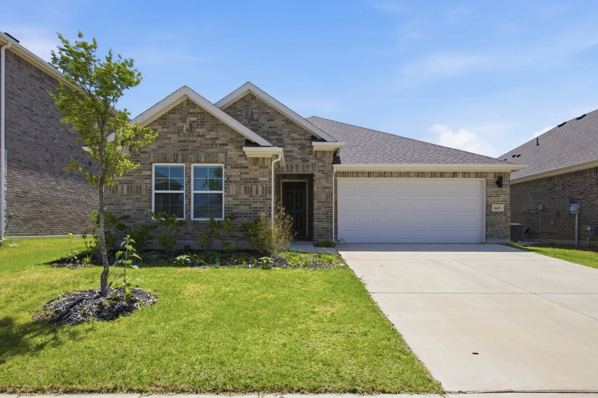Brick exterior with white trim, two-car garage, concrete driveway, and front yard landscaping