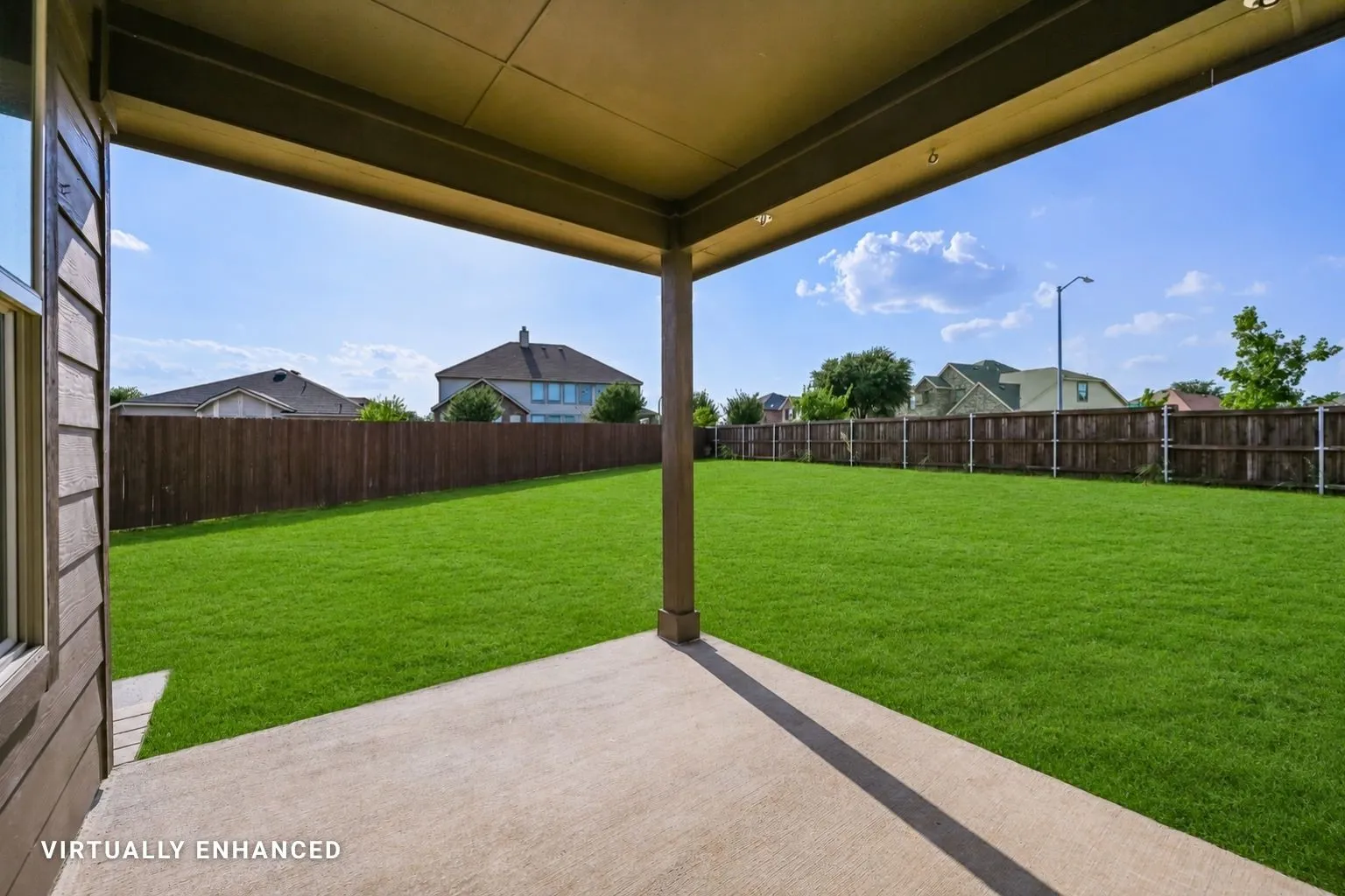 Covered patio with a concrete surface, expansive lawn, and wooden privacy fencing