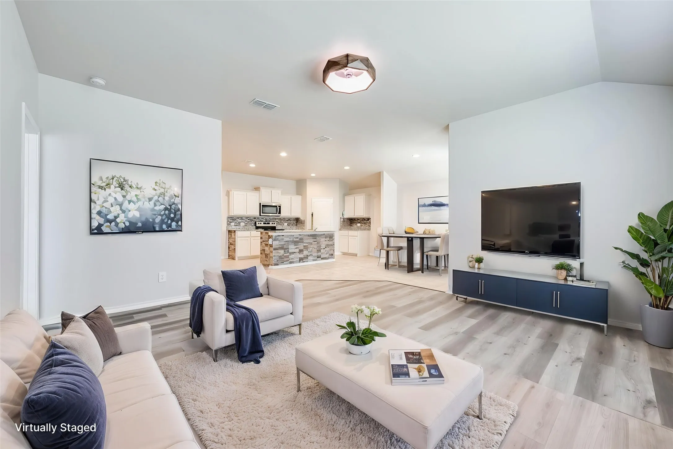 Open-concept living area featuring light wood-finish flooring, vaulted ceilings, recessed lighting, and a built-in kitchen island with stone-finish detailing