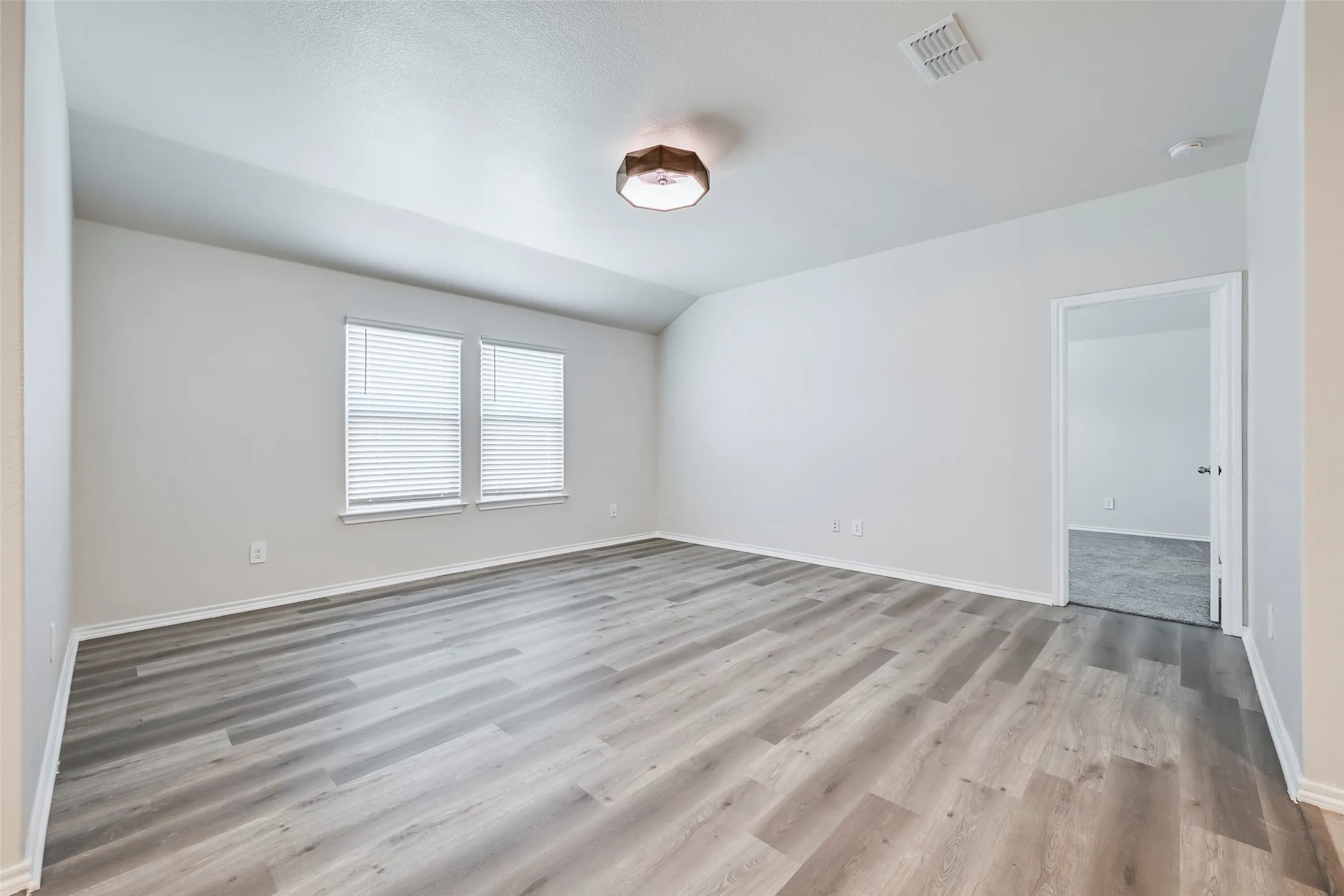 Spacious room featuring wood-finish flooring, white walls, and a ceiling-mounted light fixture
