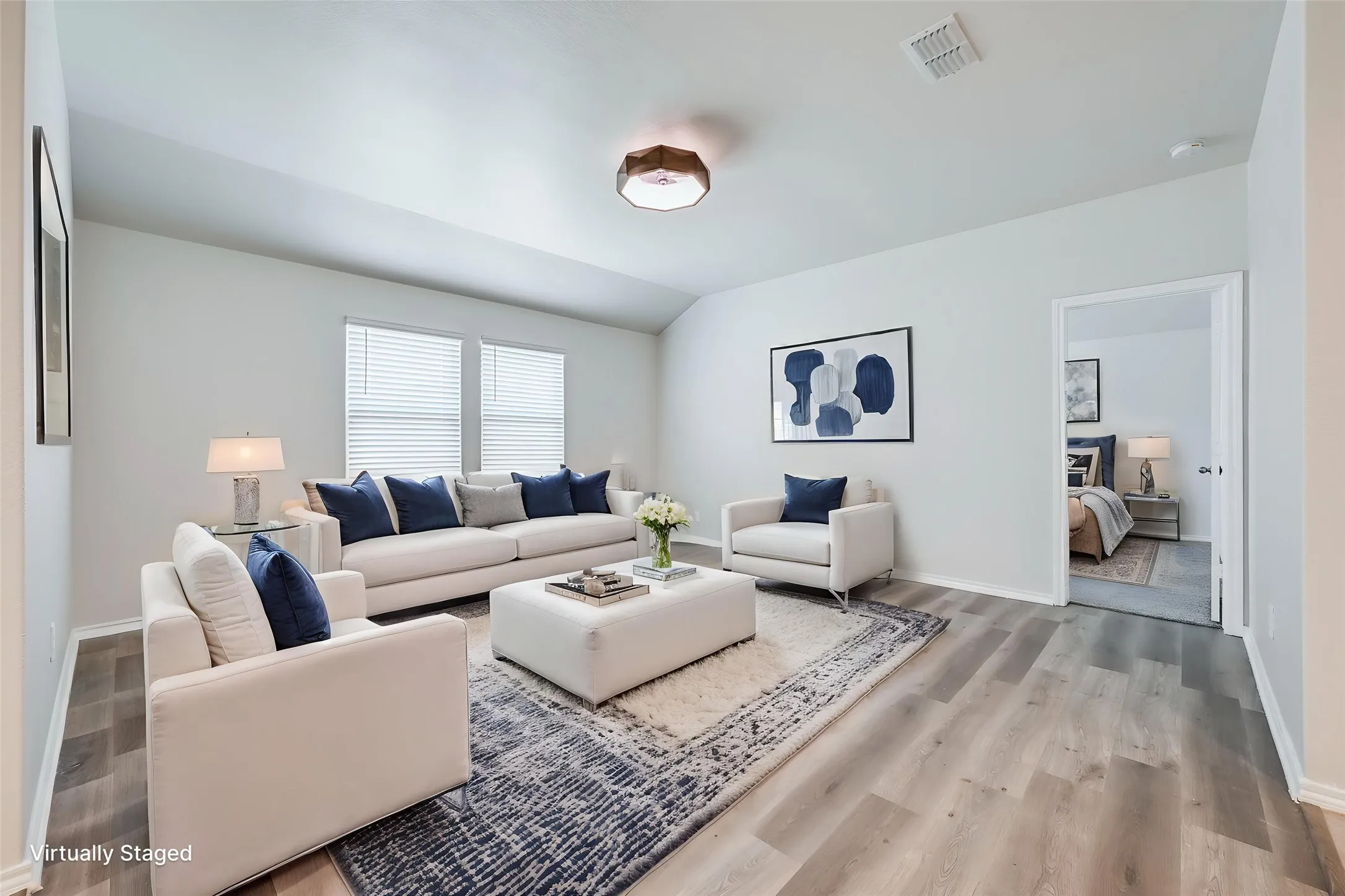 Spacious living area featuring wood-finish flooring, light neutral wall tones, and multiple windows with blinds
