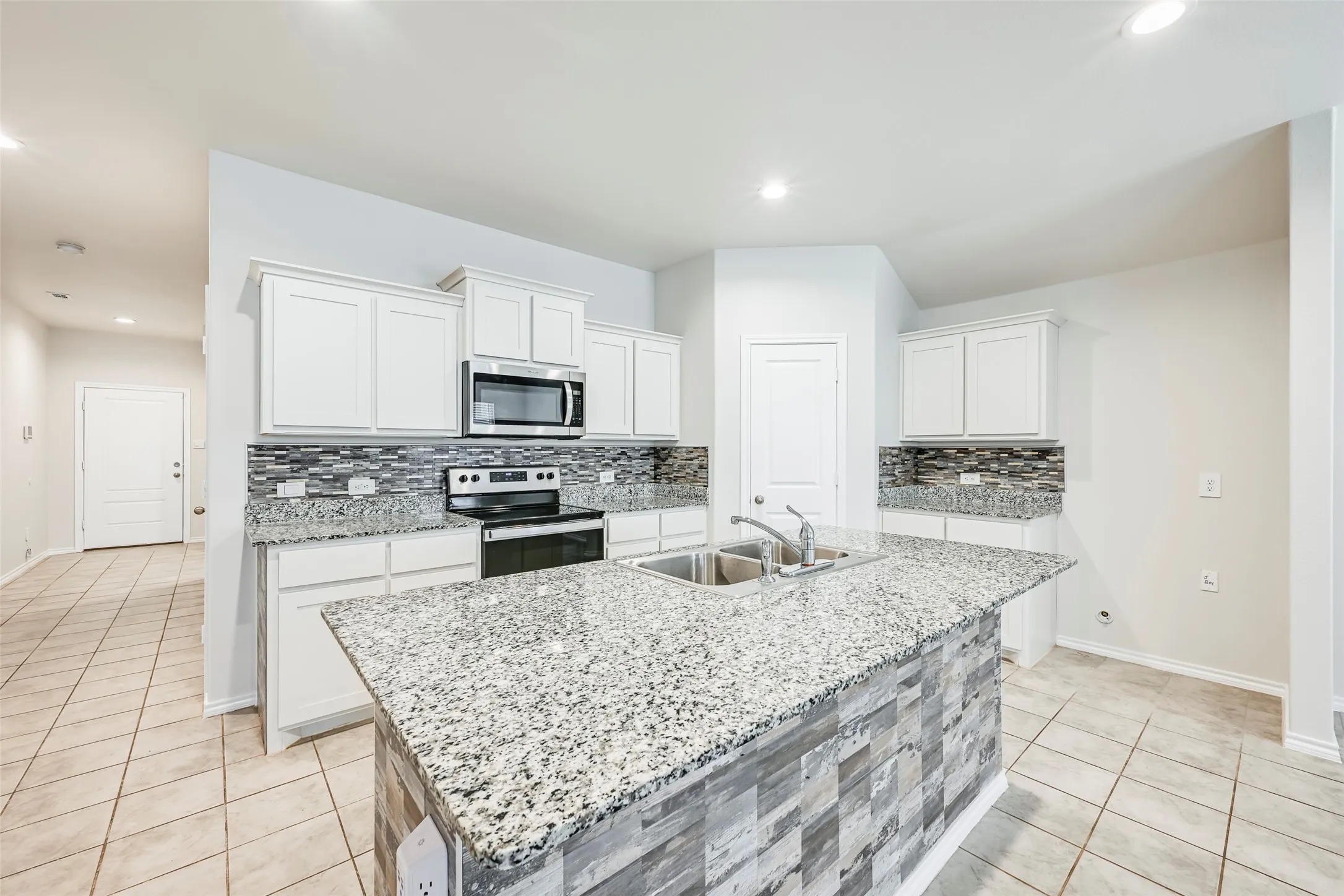 Kitchen featuring an island with a dual basin sink, white cabinetry, a mosaic tile backsplash, and granite countertops