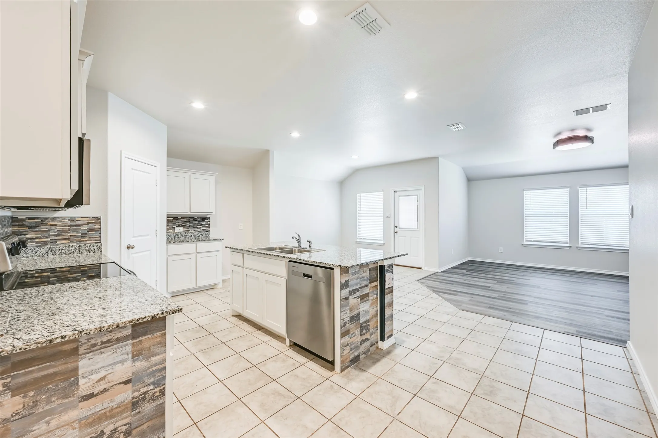 Kitchen featuring white cabinetry, granite countertops, tile flooring, and a stone-clad island with integrated stainless steel appliances