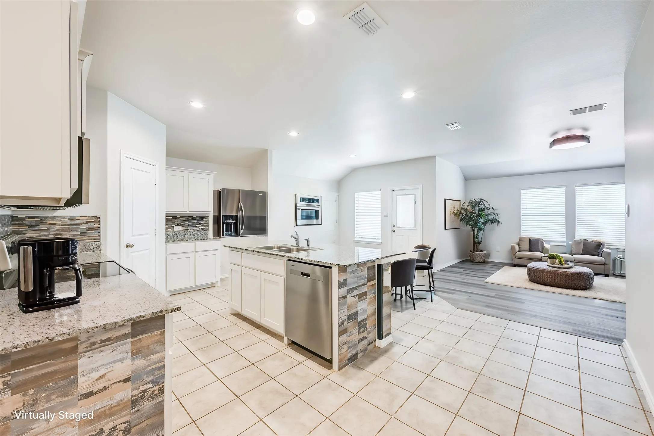Open concept kitchen featuring an island with built-in sink and dishwasher, white cabinetry, and stainless steel appliances