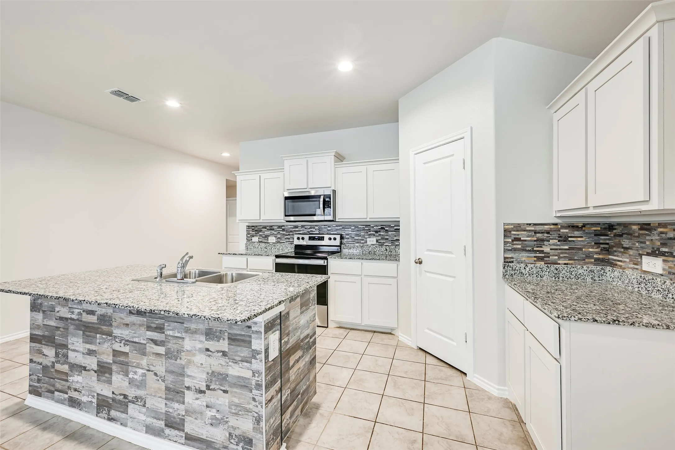 Kitchen featuring a tile floor, white cabinetry, granite countertops, tile backsplash, and a large center island with a double basin sink