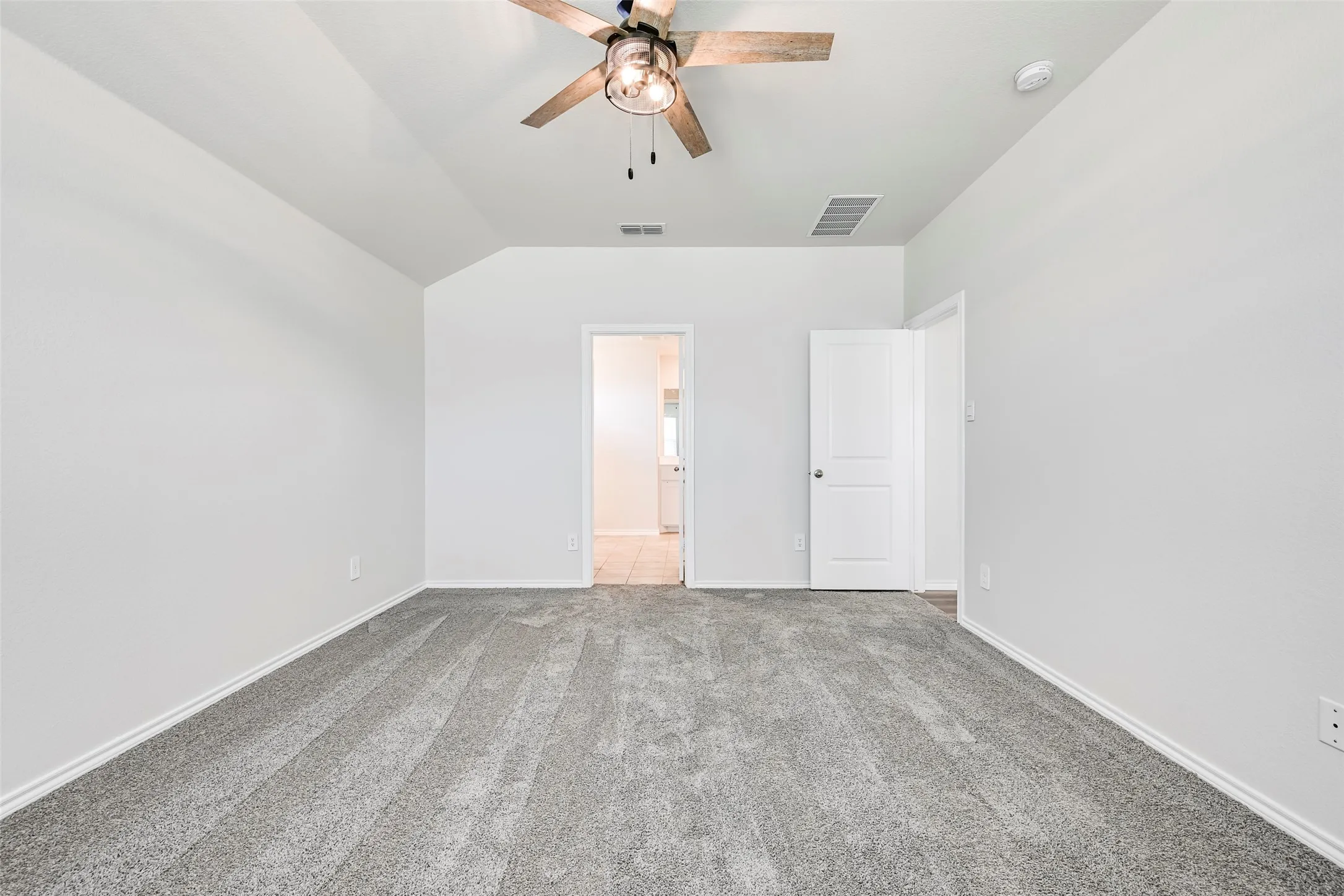 Vaulted ceiling, ceiling fan with light fixture, carpeted flooring, white interior doors, and neutral wall tones