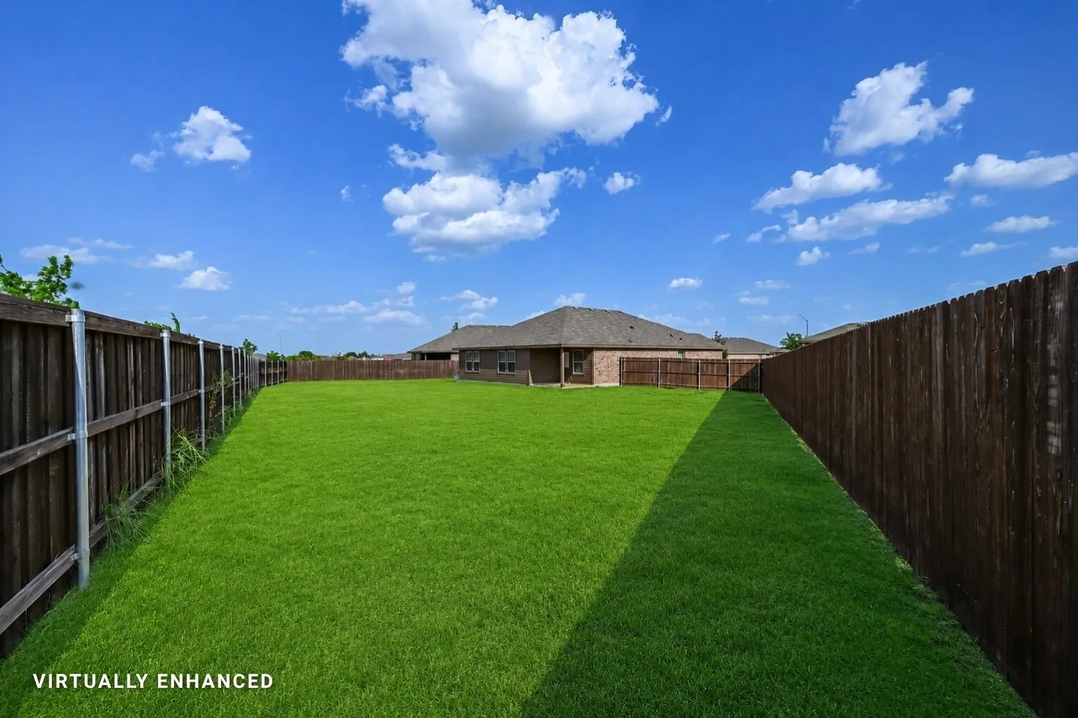 Expansive backyard with a manicured lawn, full privacy fencing, and a brick exterior dwelling