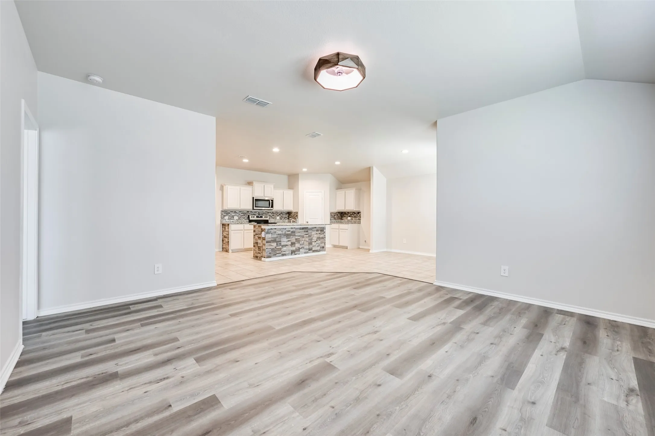 Wood-finish flooring, vaulted ceiling, recessed lighting, contemporary ceiling fixture, and a kitchen featuring a stone-clad island