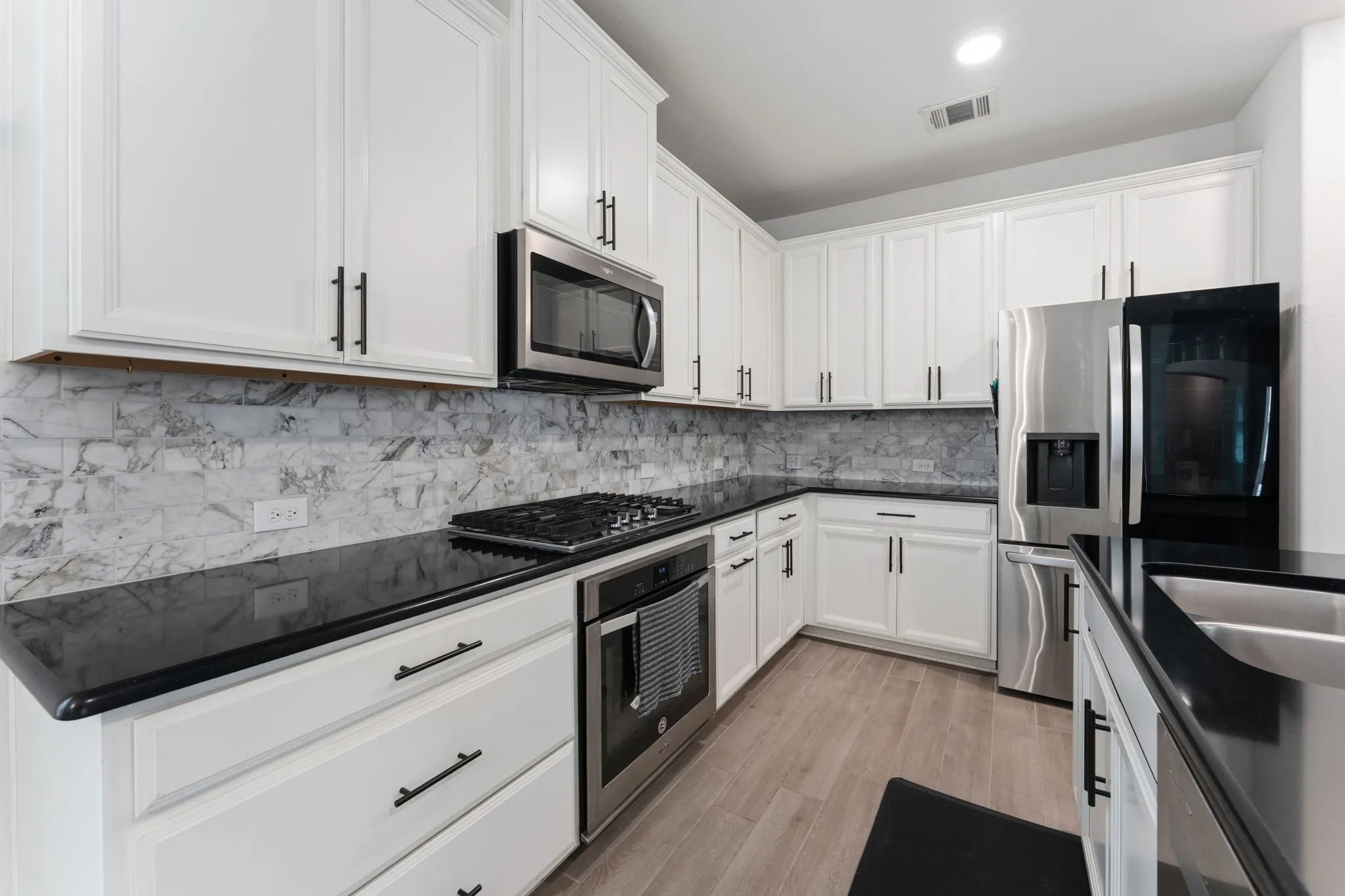 Kitchen featuring white cabinetry with matte black hardware, black countertops, stainless steel appliances including a gas range and built-in microwave, and a patterned tile backsplash