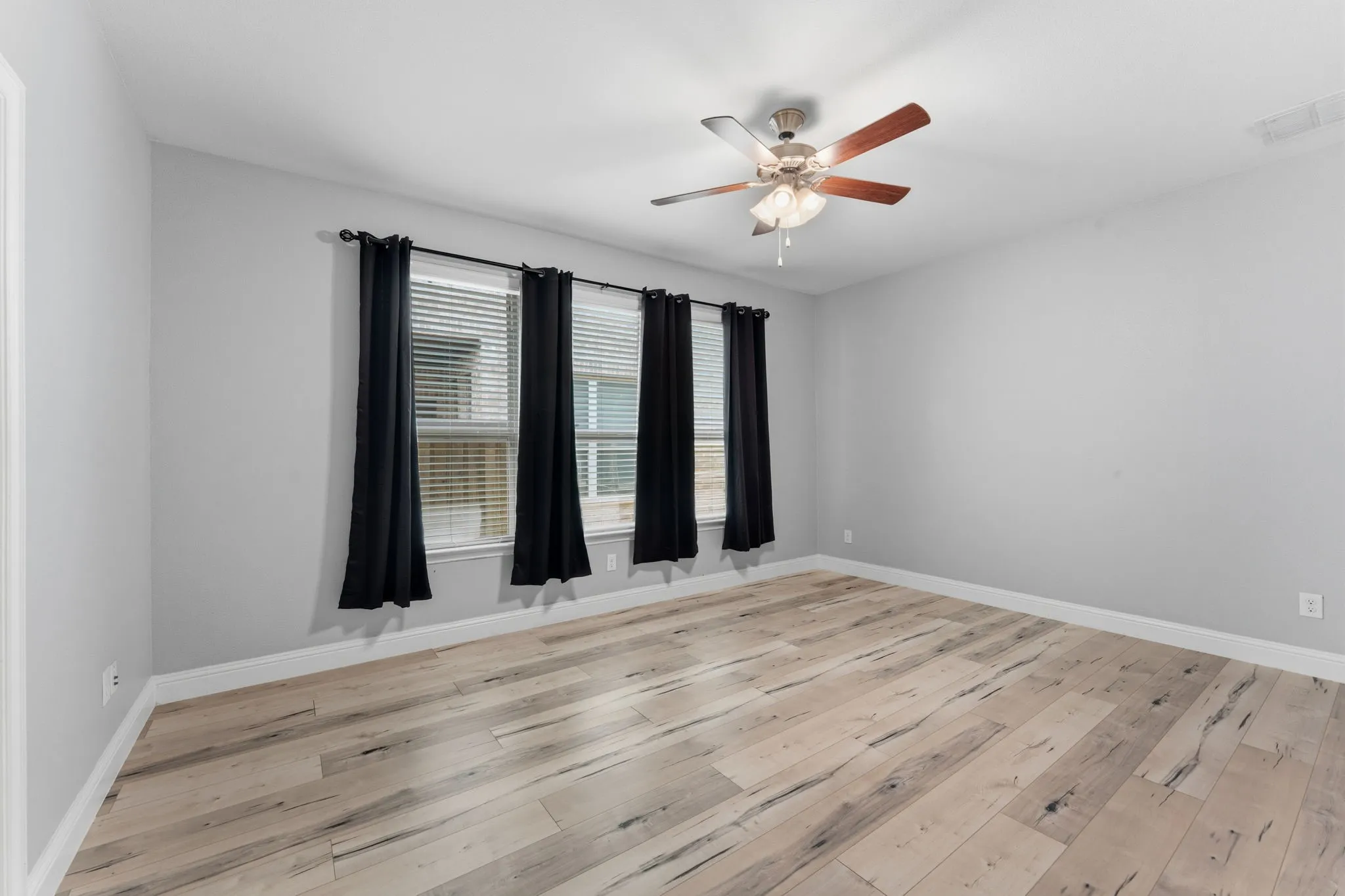 Interior room featuring light-toned wood-finish flooring, light gray wall paint, and white baseboards