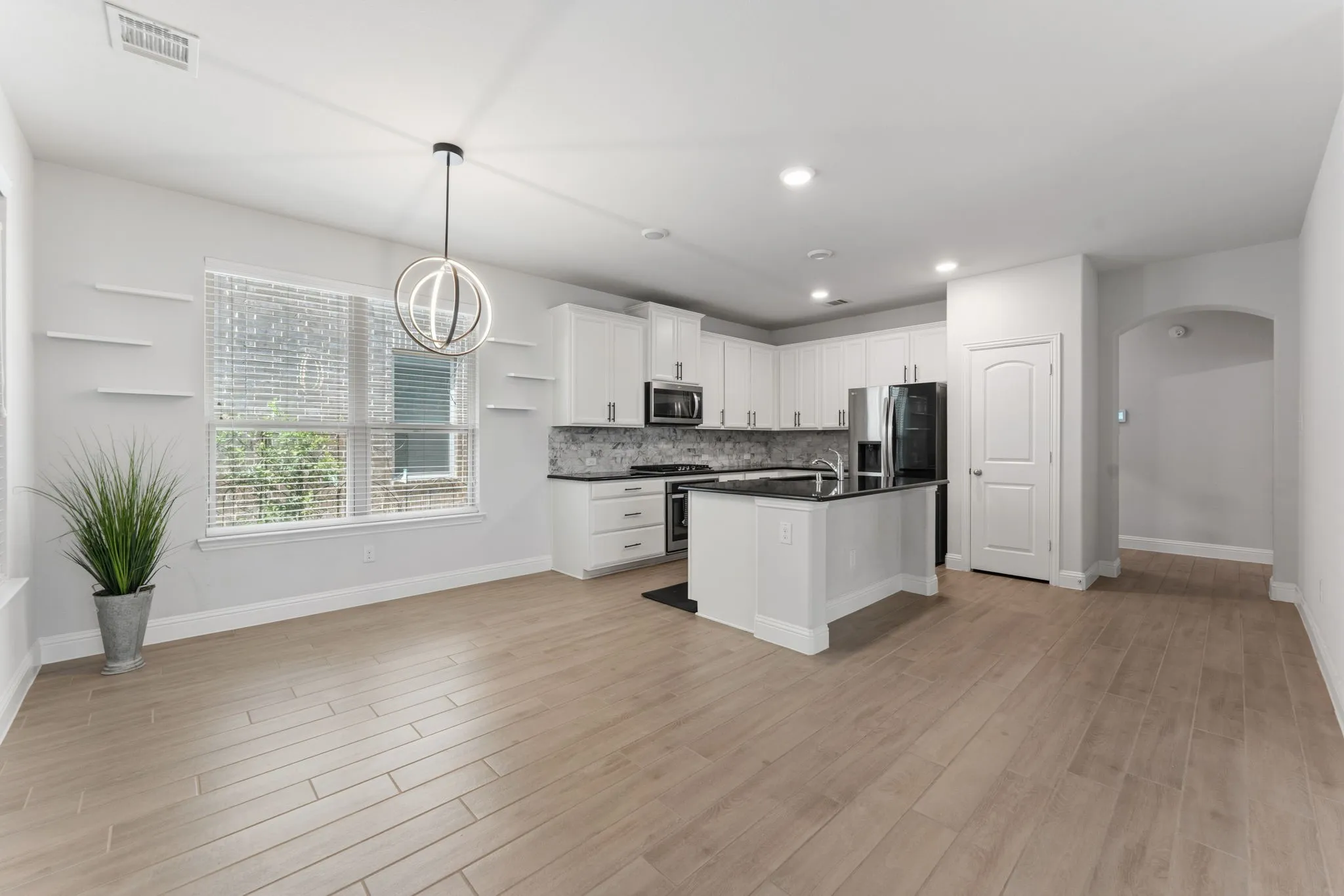 Open-concept living space featuring wood-finish flooring, a contemporary kitchen with white cabinetry and dark countertops, a central island, and a modern pendant light fixture