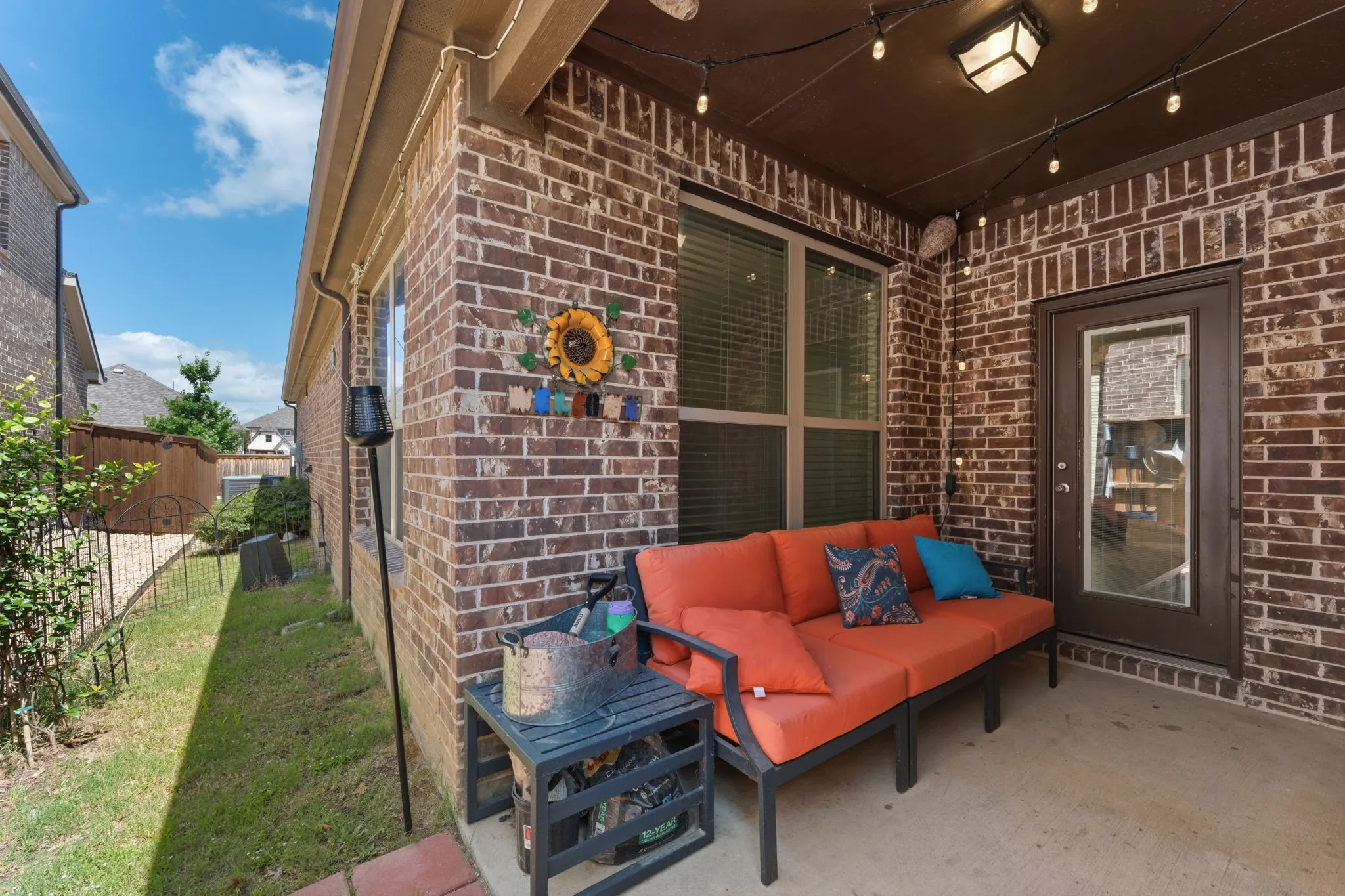 Covered patio with brick siding, string lighting, recessed ceiling fixture, and a glass-paneled exterior door