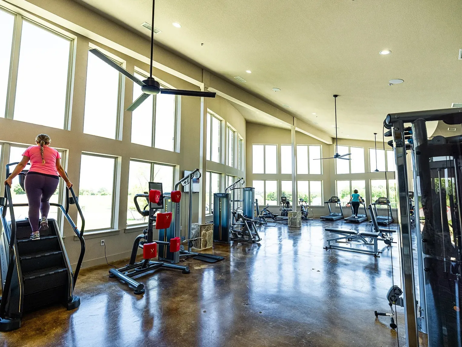 Fitness center featuring high ceilings, extensive window banks, multiple ceiling fans, recessed lighting, and polished concrete flooring