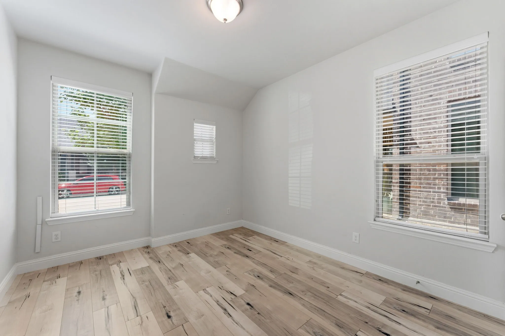 Light wood-finish flooring throughout this room, featuring three windows with blinds