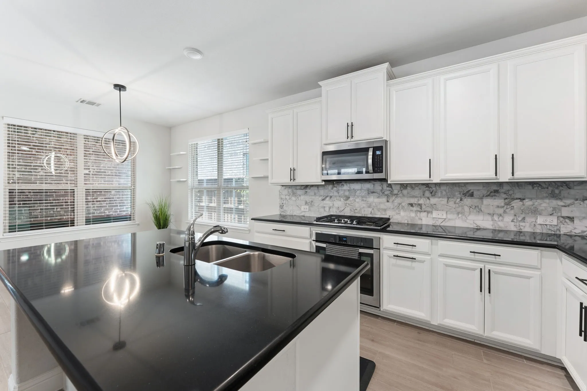 Kitchen featuring a large island with an integrated sink, dark solid surface countertops, white cabinetry with black hardware, a tile backsplash, and stainless steel appliances