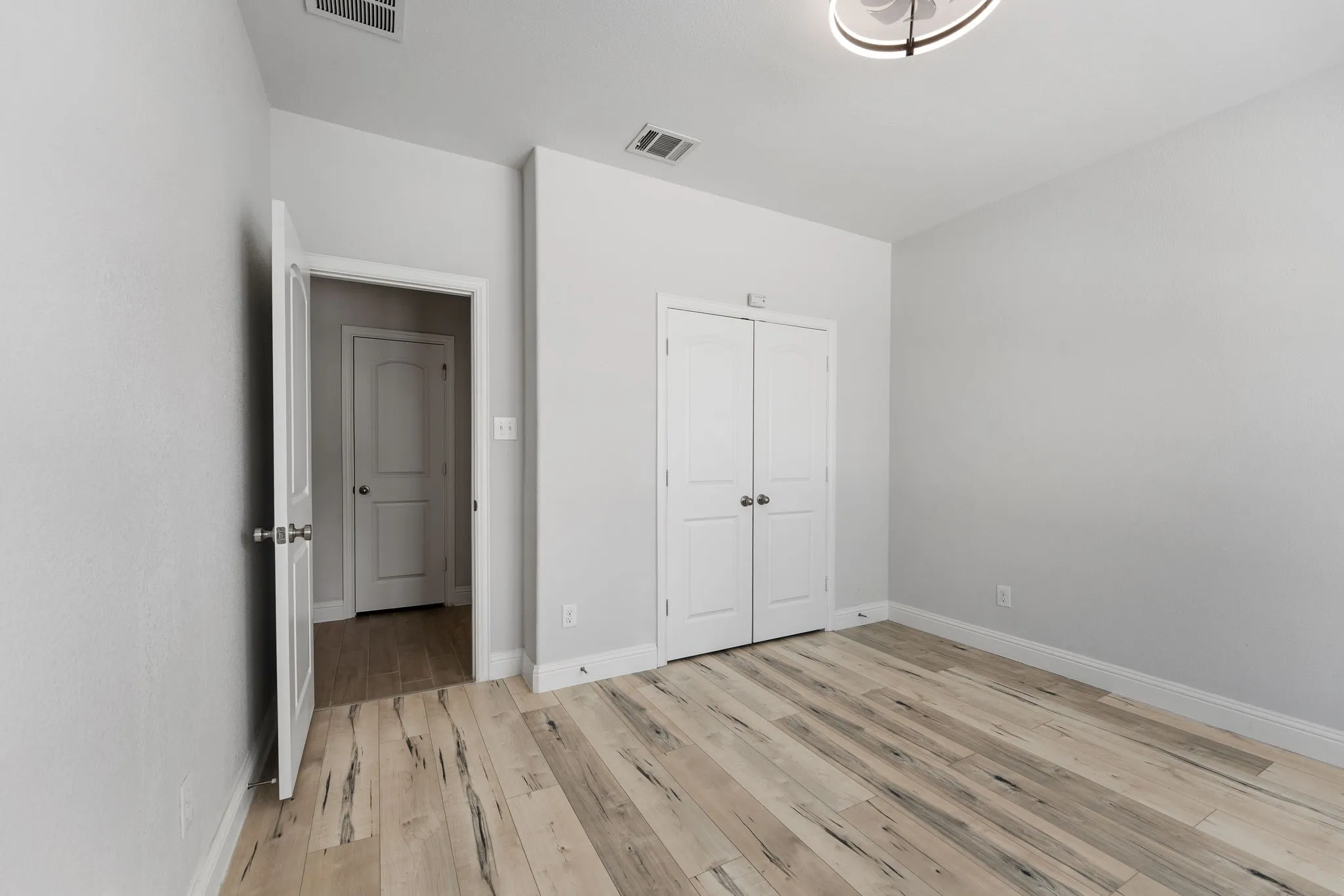 Room with light wood-finish flooring, white walls, and a modern ceiling light fixture
