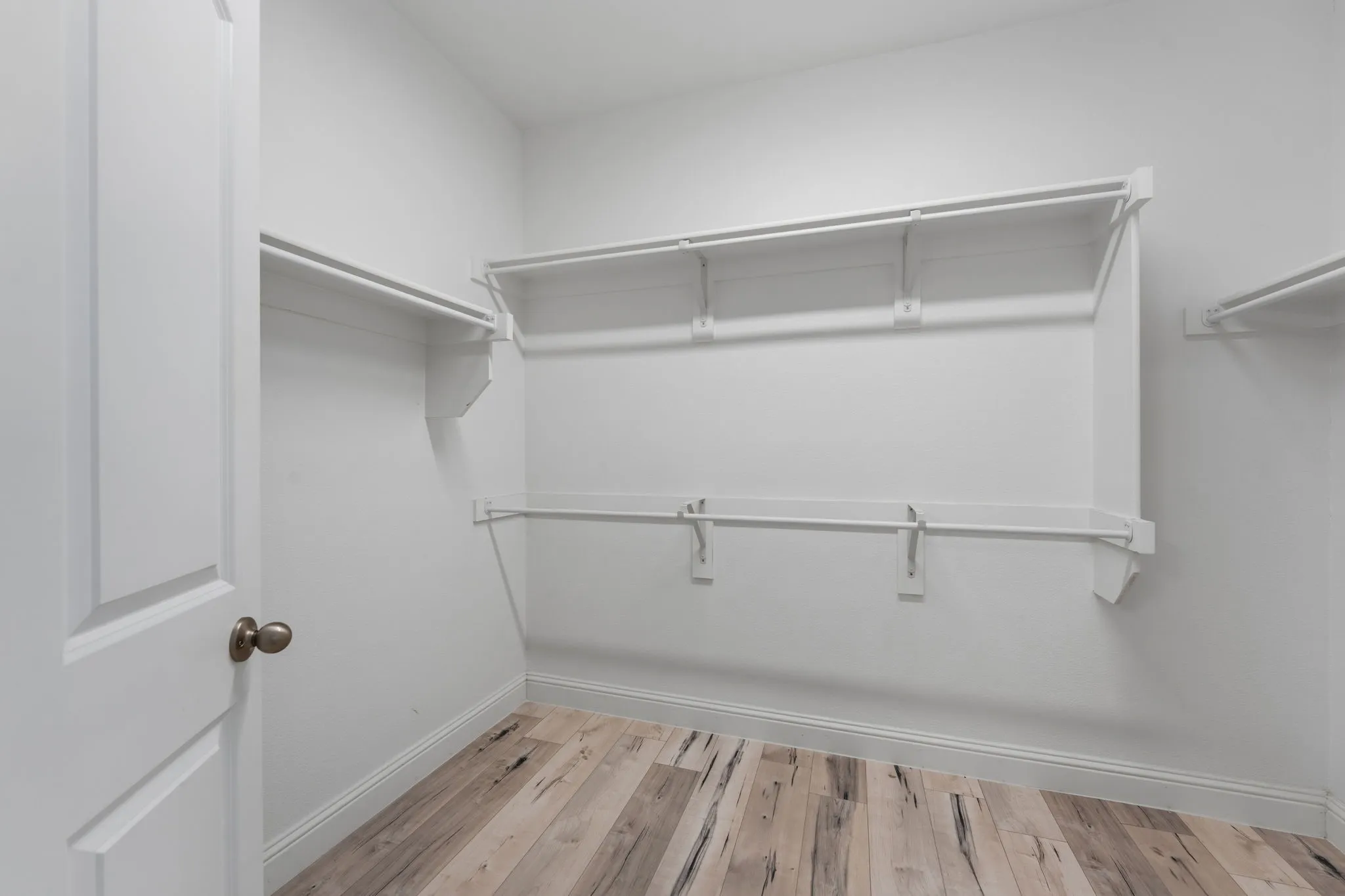Spacious walk-in closet featuring white built-in shelving and hanging rods