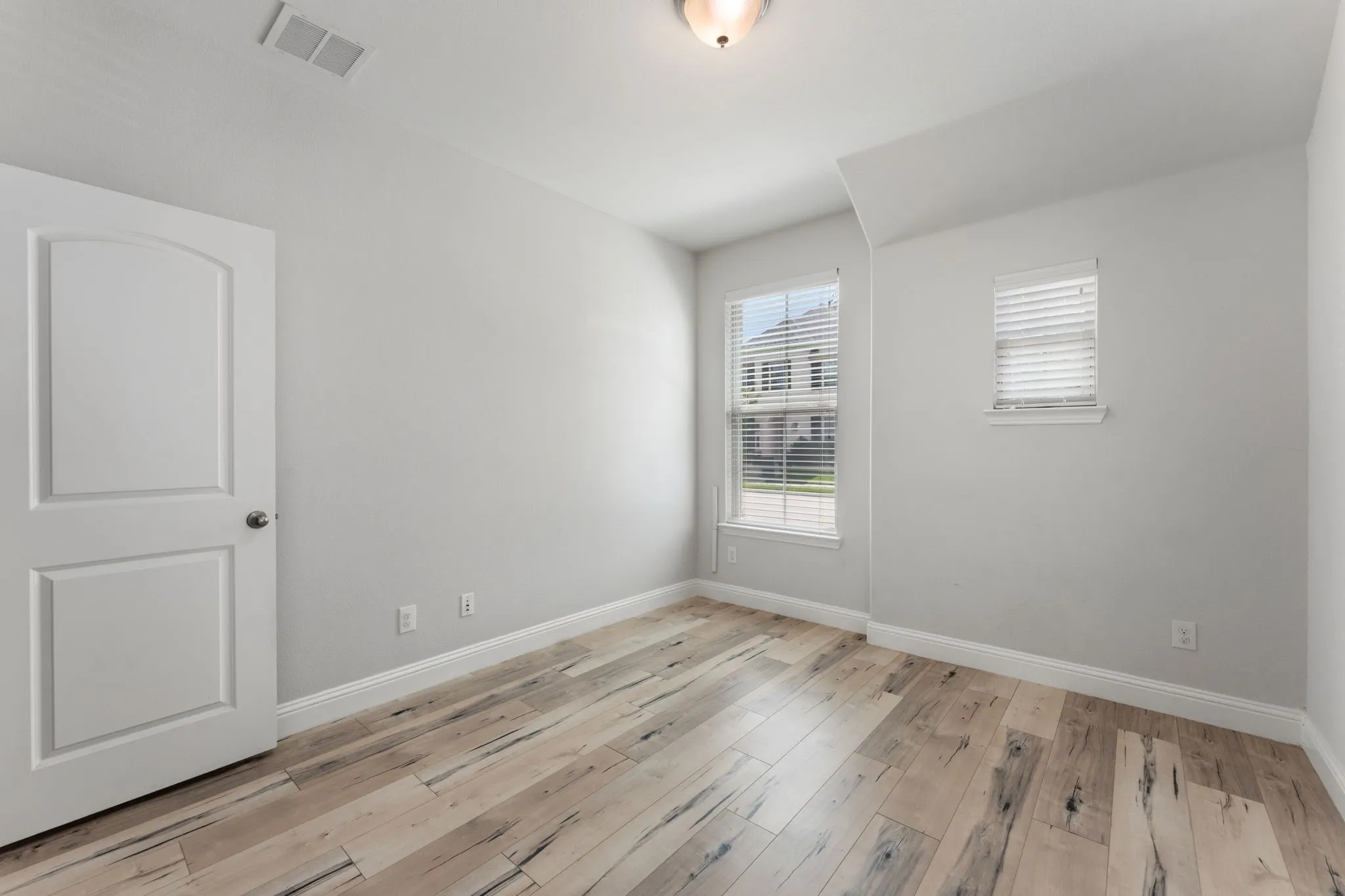 Spacious room featuring wood-finish flooring, light grey walls, and two windows with white blinds