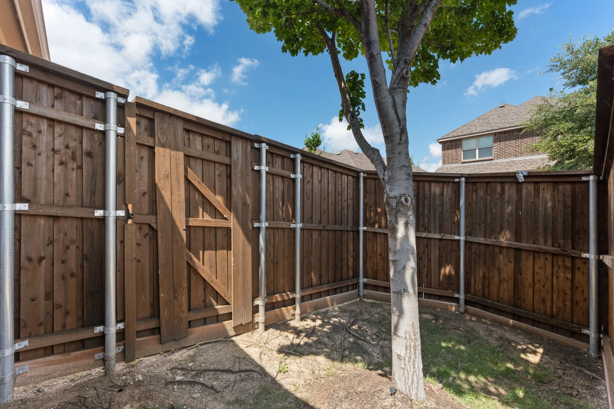 Private backyard featuring a wood fence with metal posts, a small gate, and a mature tree
