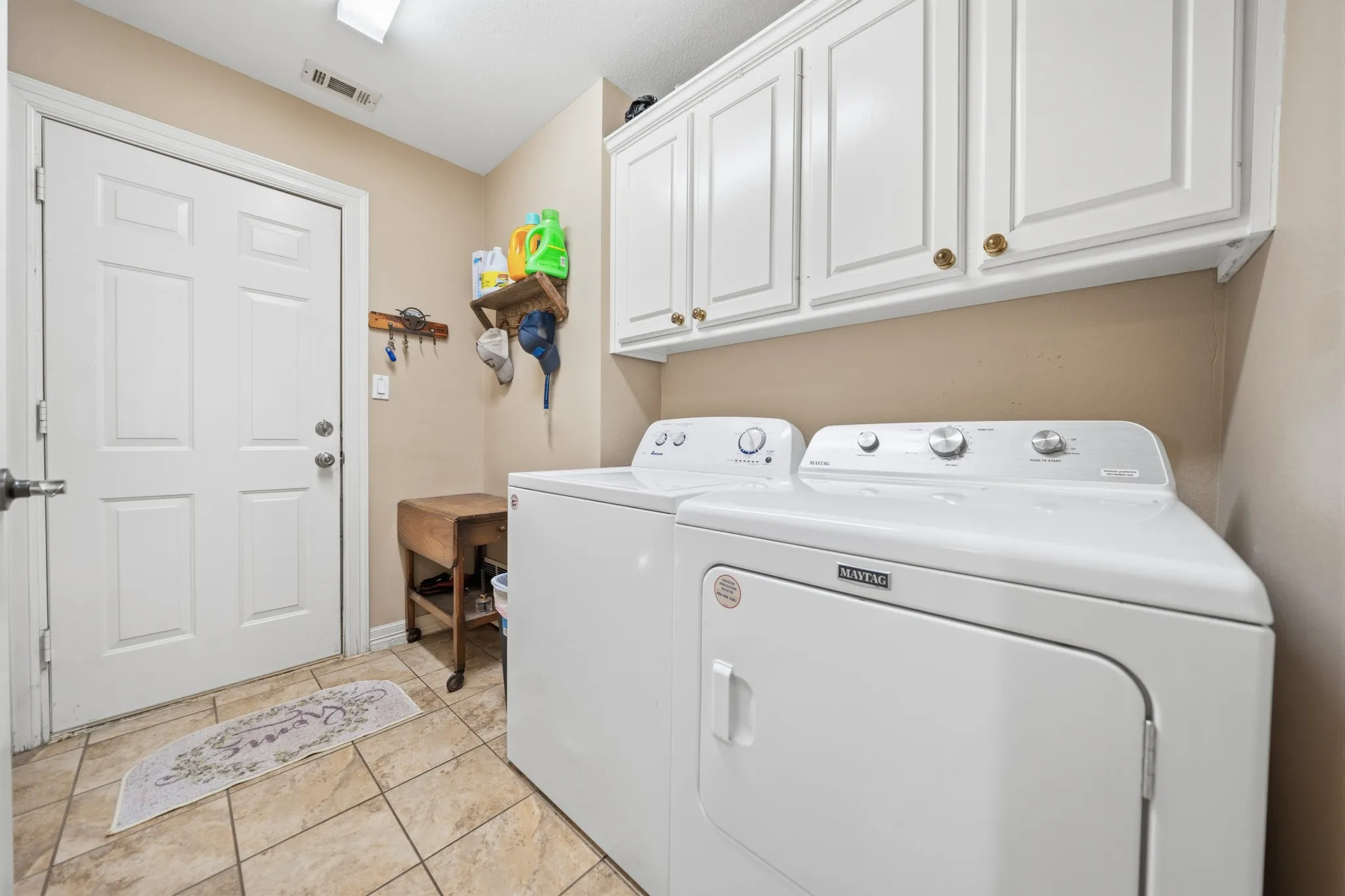 White paneled door, tiled flooring, white upper cabinetry with brass hardware, and a ceiling-mounted light fixture