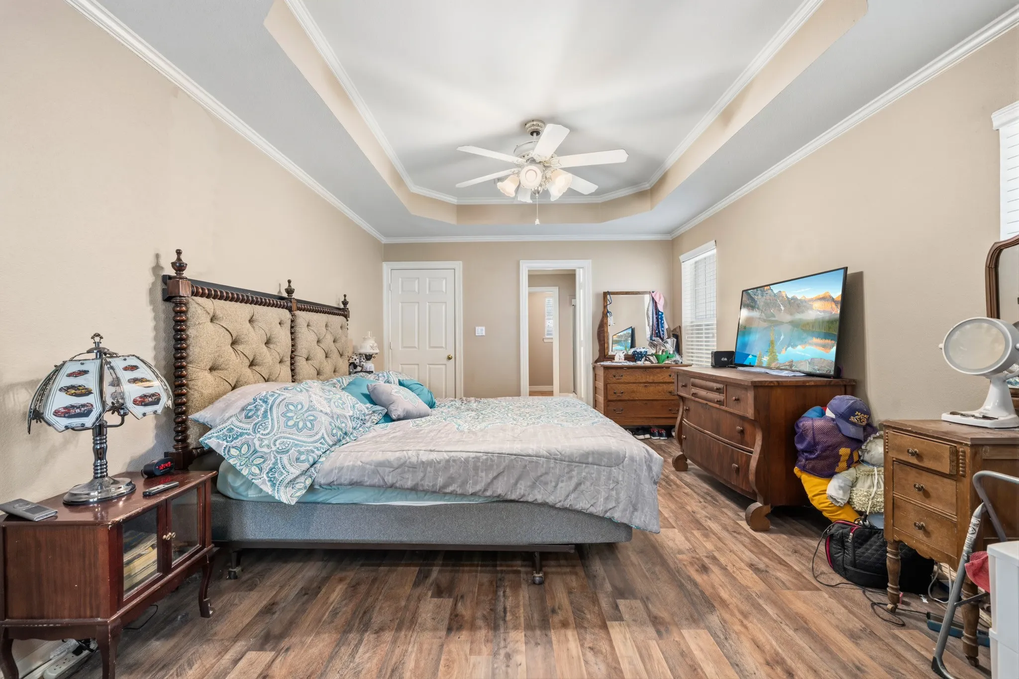 Tray ceiling with a ceiling fan, wood-finish flooring, two windows with blinds, and light-toned walls