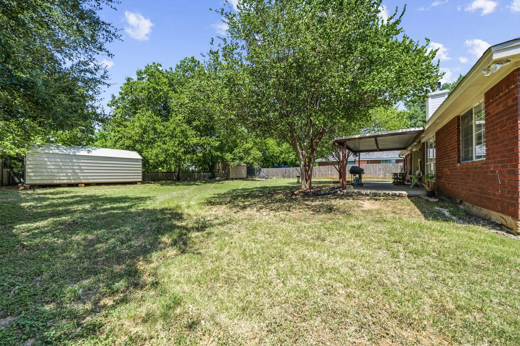 Expansive backyard featuring a mature tree, covered patio, and brick exterior