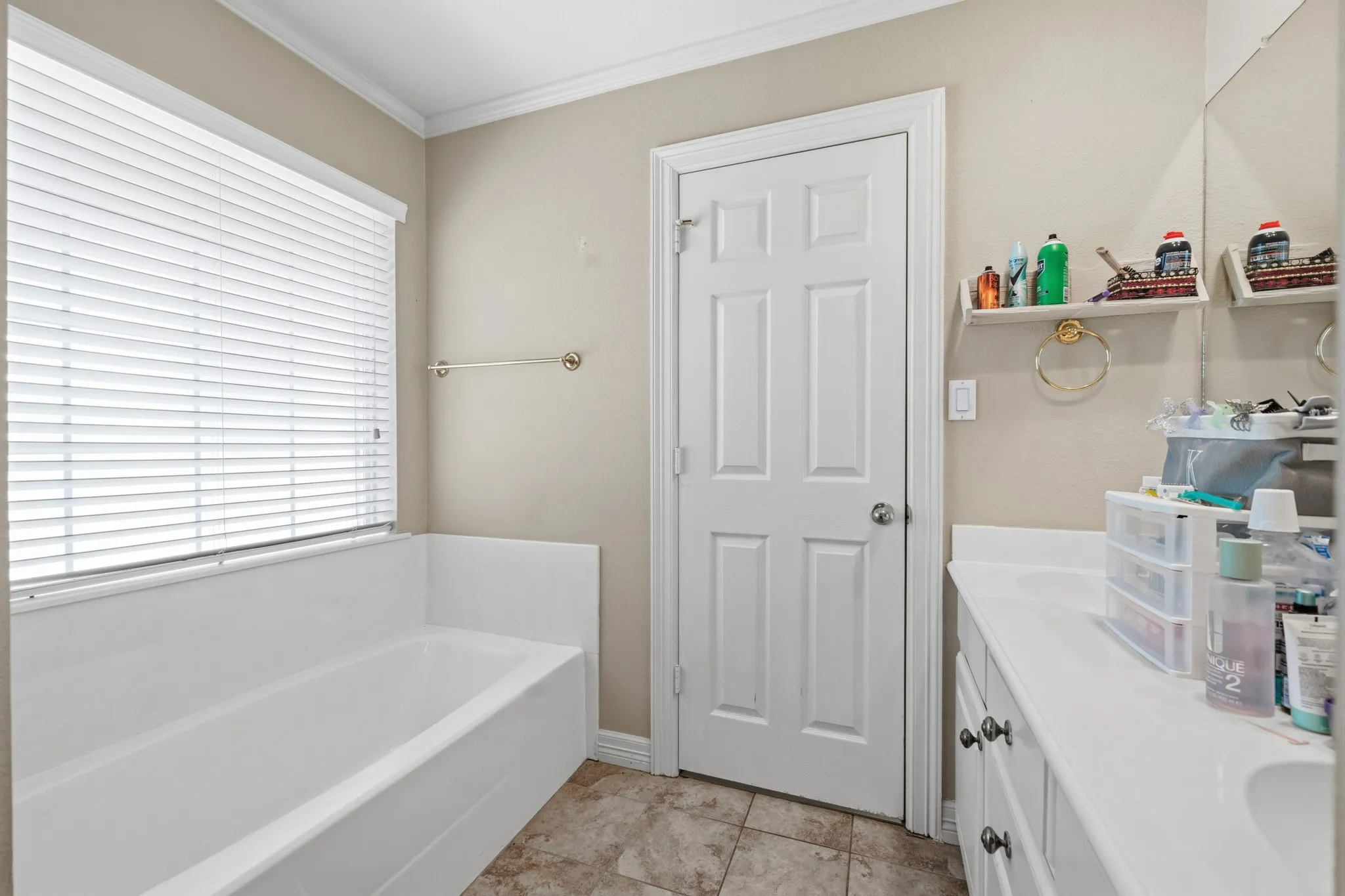 White paneled door with chrome hardware, white bathtub, and light-colored wall with white crown molding