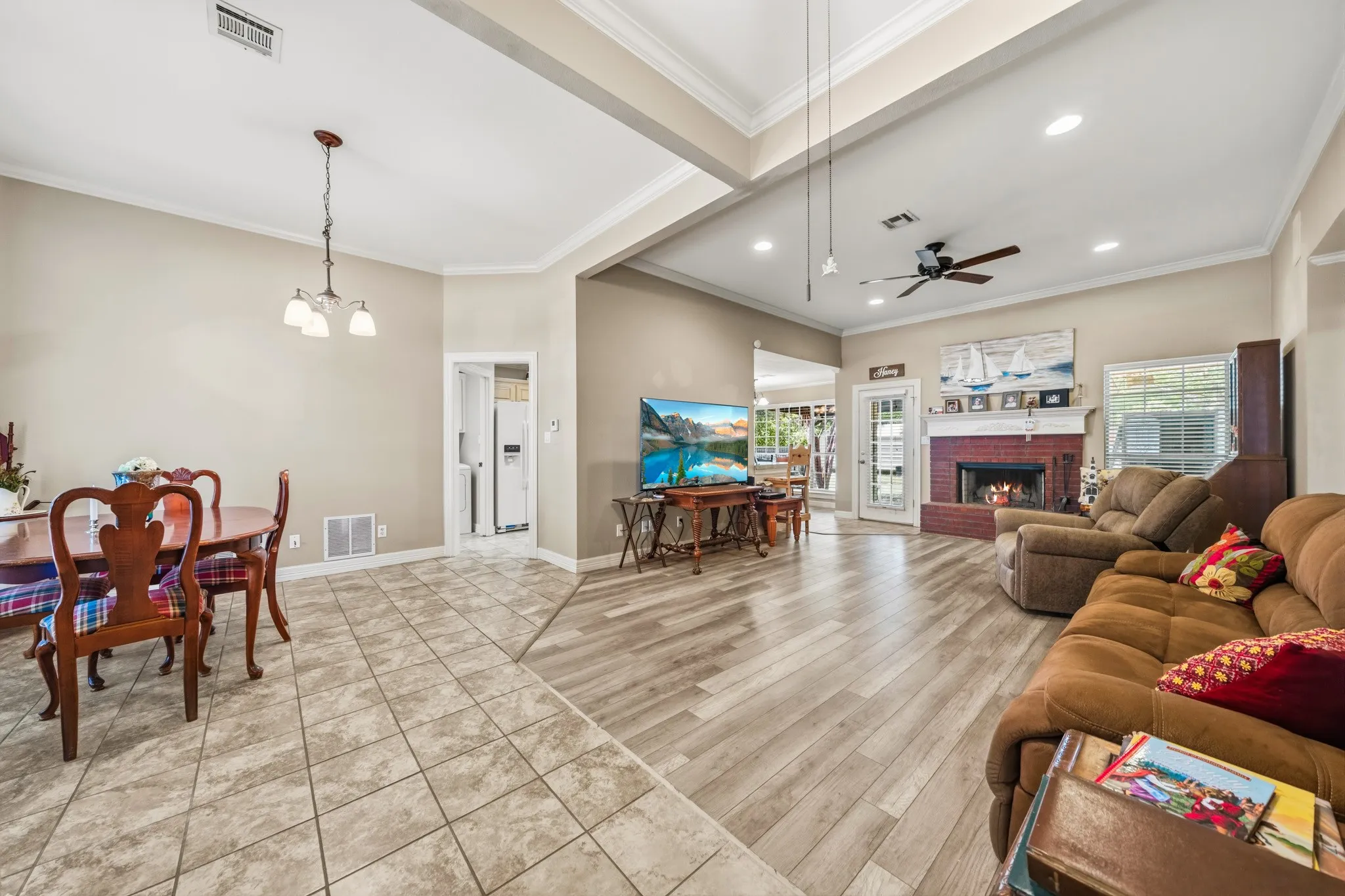 Open concept living space featuring wood-finish flooring, a brick fireplace with a white mantel, and a ceiling fan