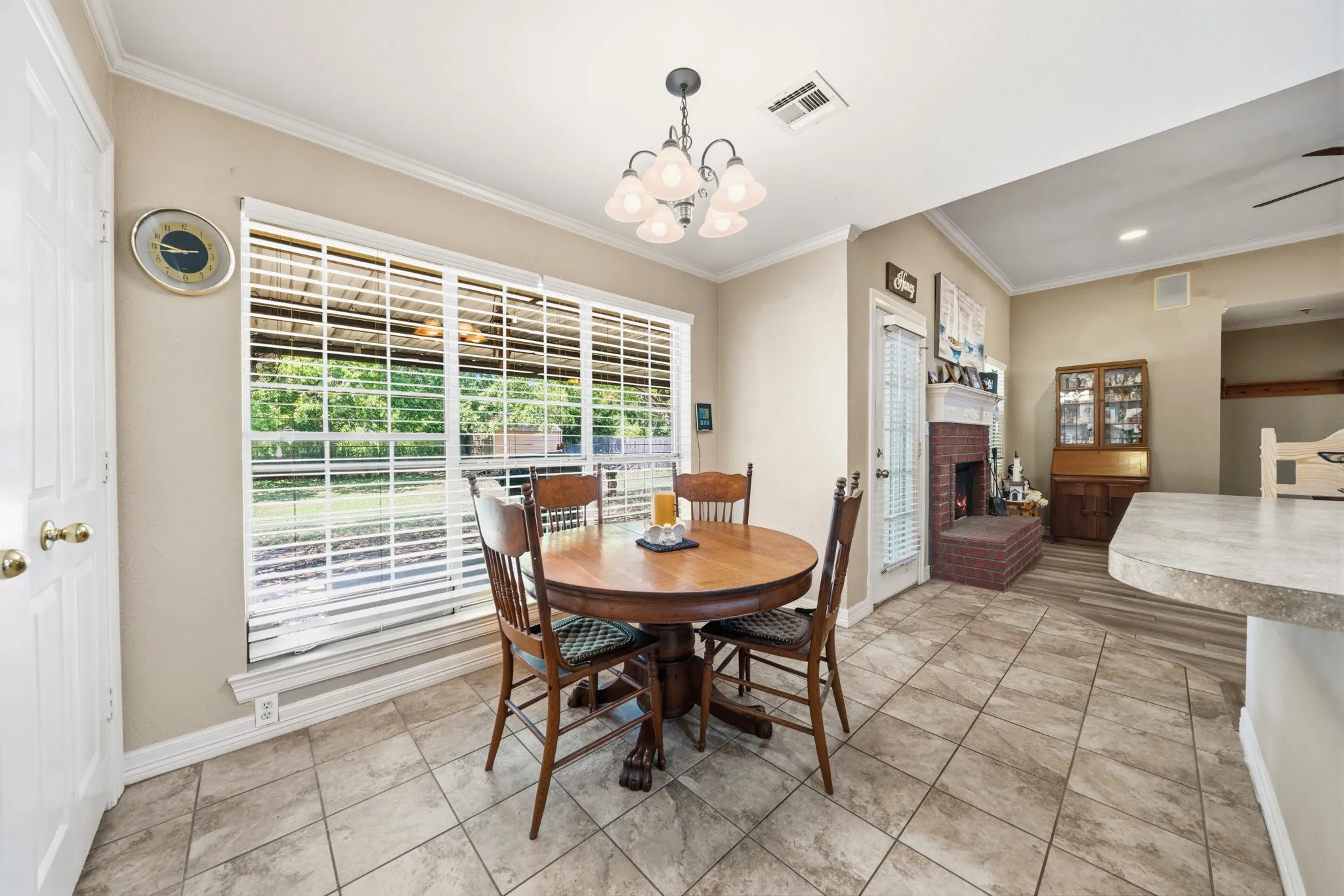 Expansive window with blinds, tile flooring, built-in fireplace with brick surround, vaulted ceiling, and built-in cabinetry