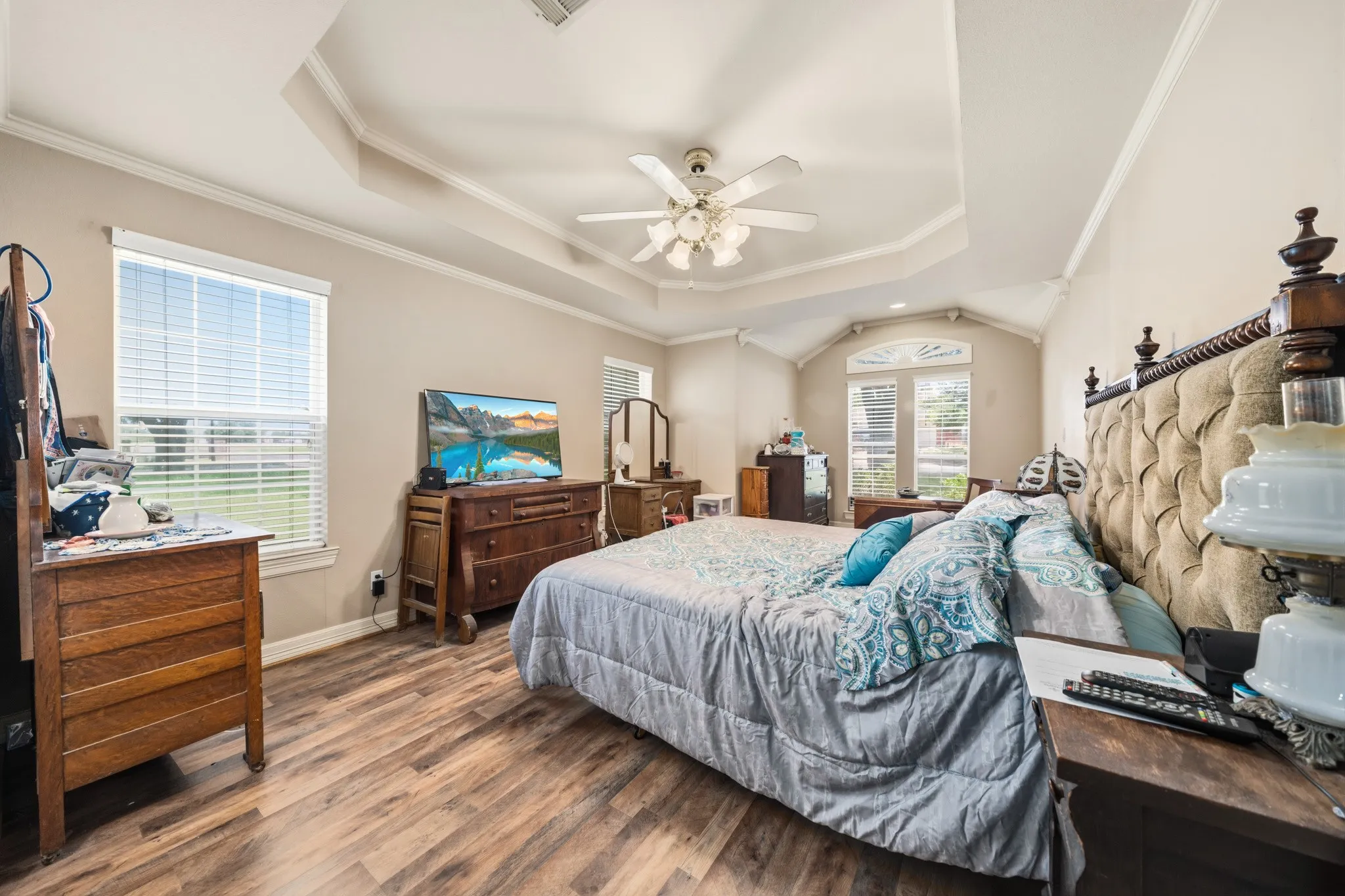 Tray ceiling with crown molding, wood-finish flooring, ceiling fan, and arched window