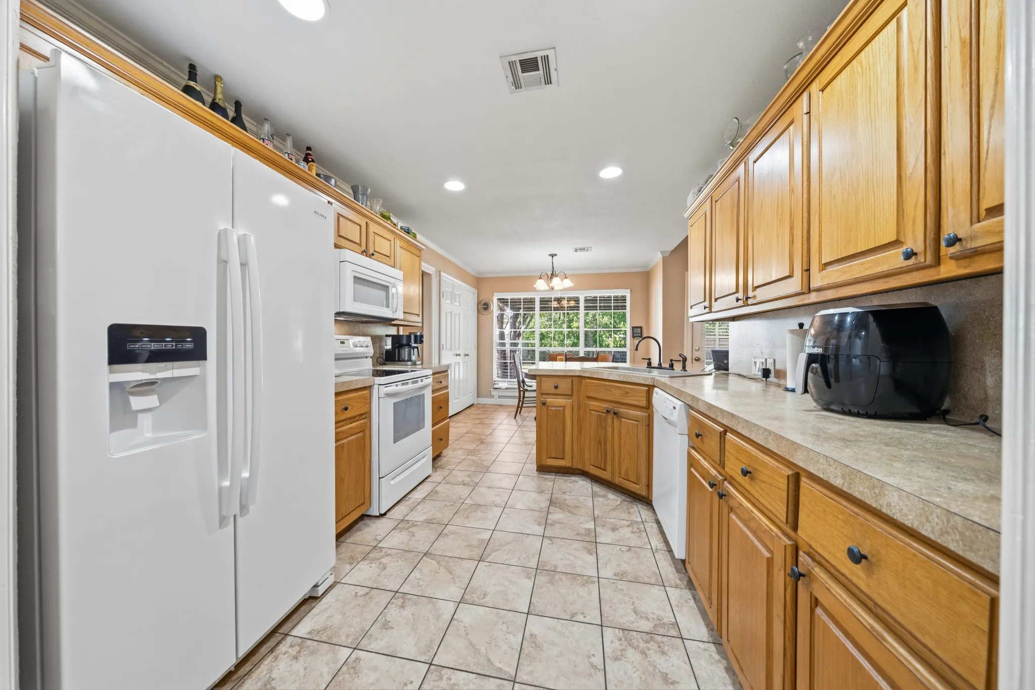 Galley kitchen featuring wood cabinetry, integrated white appliances, and tiled flooring