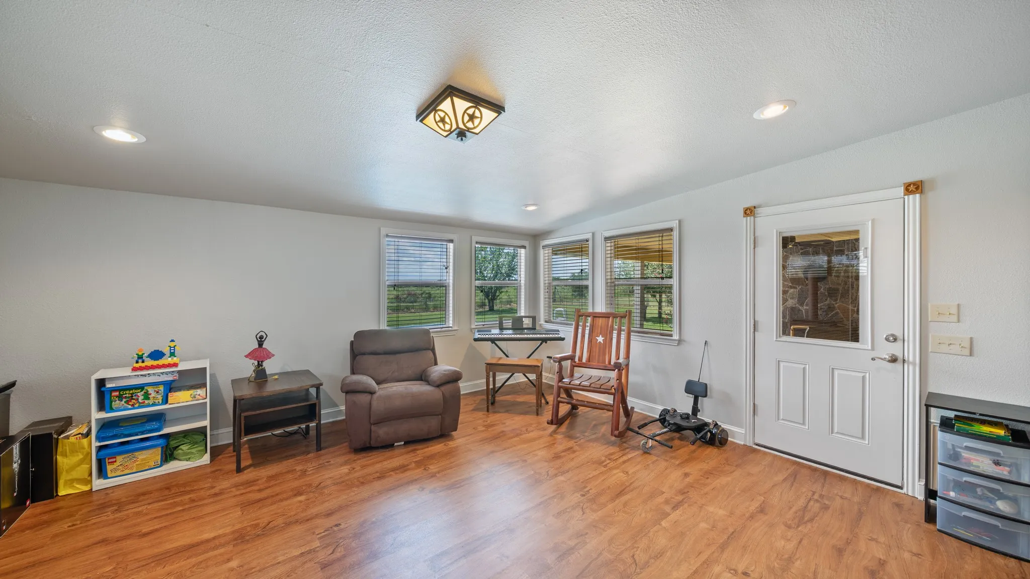 Bright, open sunroom featuring wood-finish flooring, large multi-pane windows with natural light throughout, recessed ceiling lighting, and direct access to exterior spaces via glass doors
