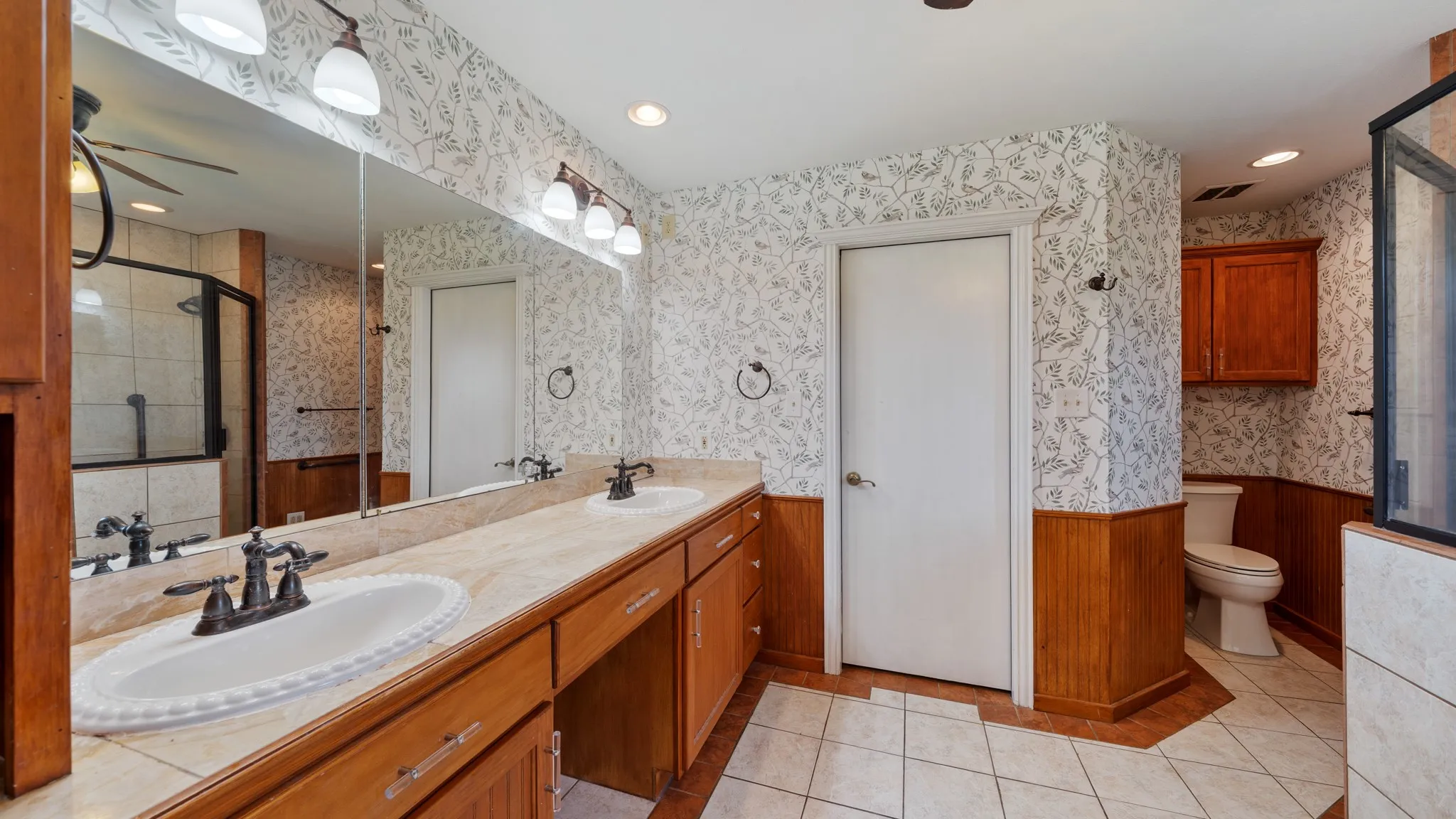 Primary bathroom featuring dual vanities with wood cabinetry, marble countertops, and polished nickel fixtures