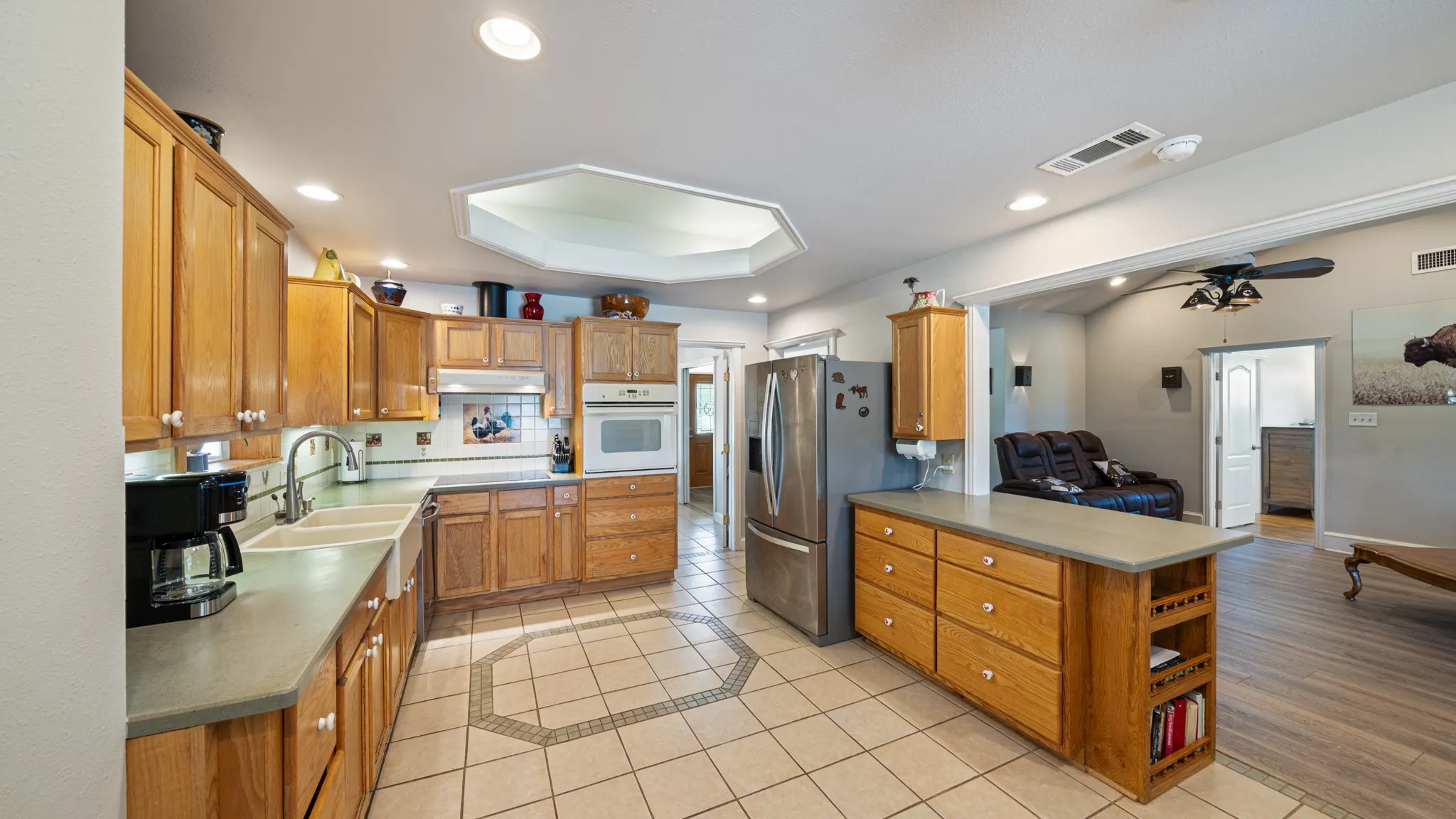 Spacious chef's kitchen featuring warm wood cabinetry, stainless steel appliances including a French-door refrigerator, tile countertops, and a large center island with storage