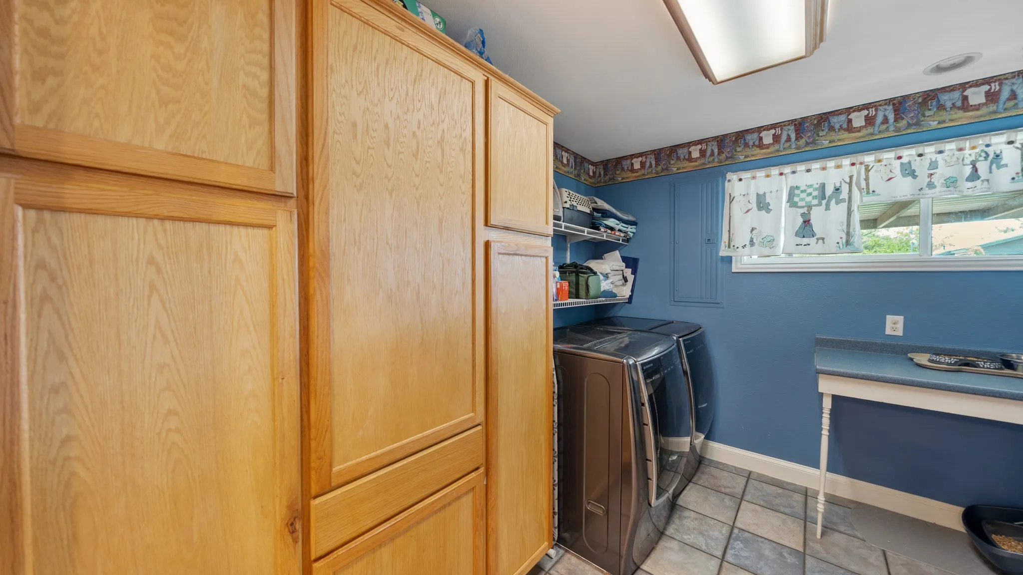 Laundry room featuring warm wood-finish cabinetry with recessed panel doors, ceramic tile flooring, and abundant storage