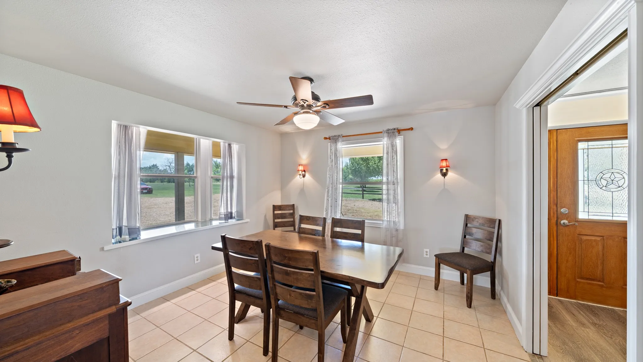 Bright dining area featuring tile flooring, a ceiling fan with integrated lighting, large windows with natural light, and direct access to adjacent spaces through French doors and a wood-trimmed entry portal